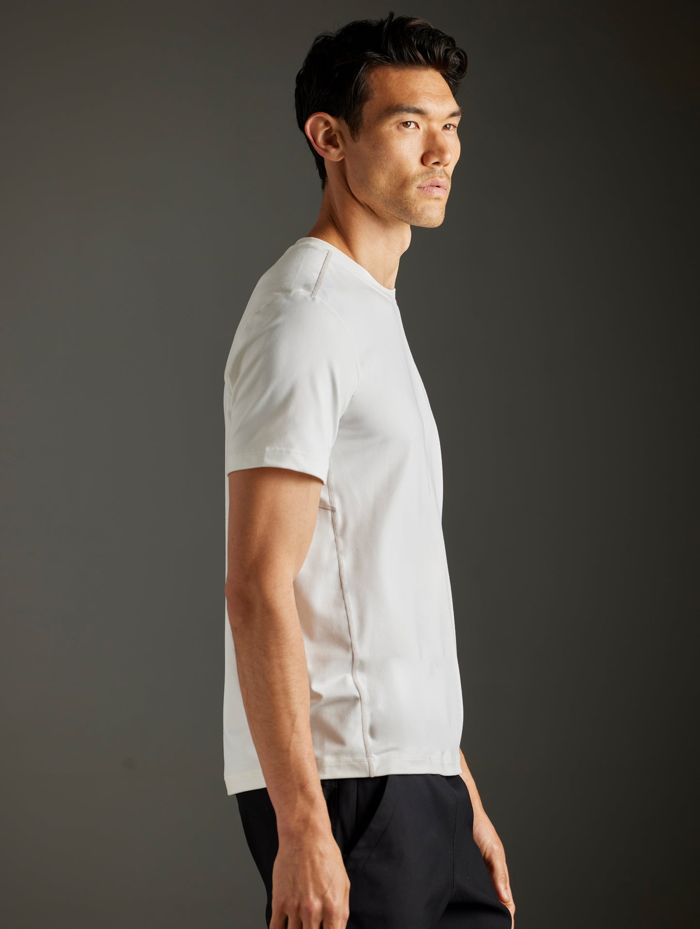 Side profile body view of man wearing Trek Articulated Tee in Natural White from AETHER Apparel.
