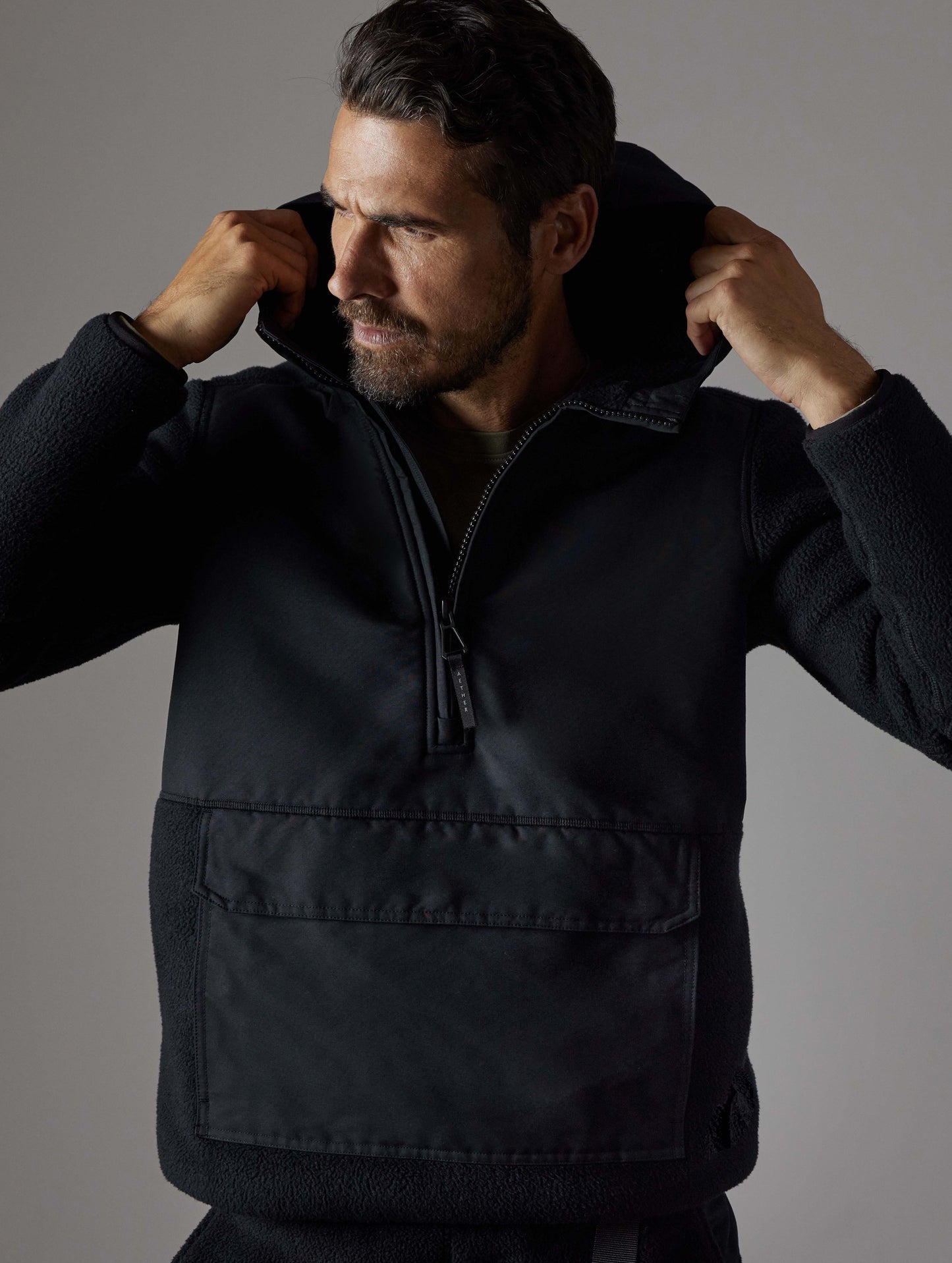 Front body view of man putting on hood of Walsh Hooded Anorak in Onyx Black from AETHER Apparel.