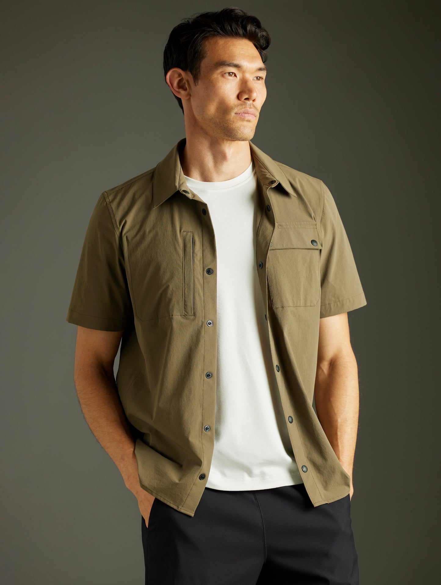 Front 3/4 body view of man wearing unbuttoned Wonder Technical Short-Sleeve Button-Down in Cadet green from AETHER Apparel.