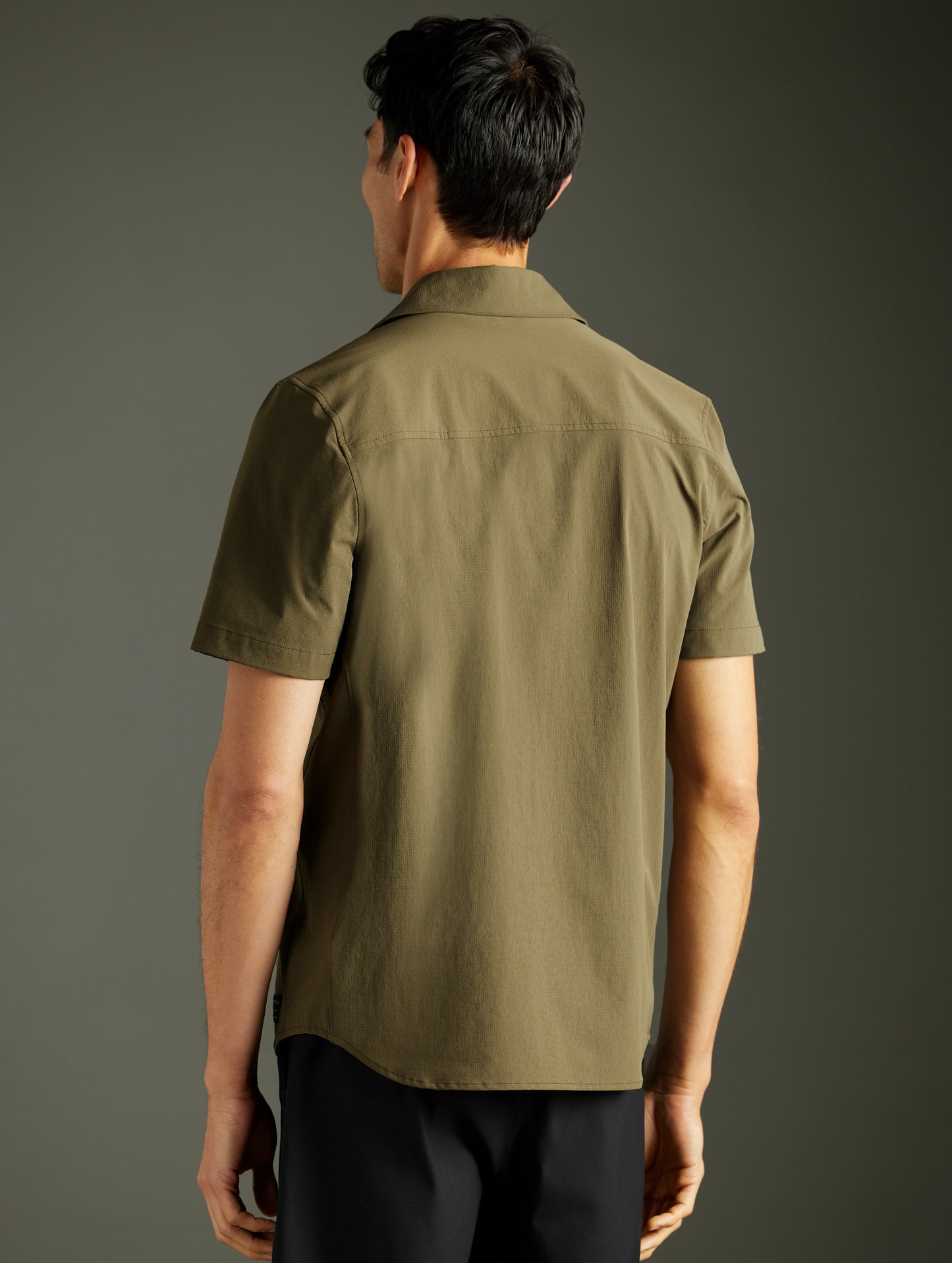 Rear 3/4 body view of man wearing Wonder Technical Short-Sleeve Button-Down in Cadet green from AETHER Apparel.