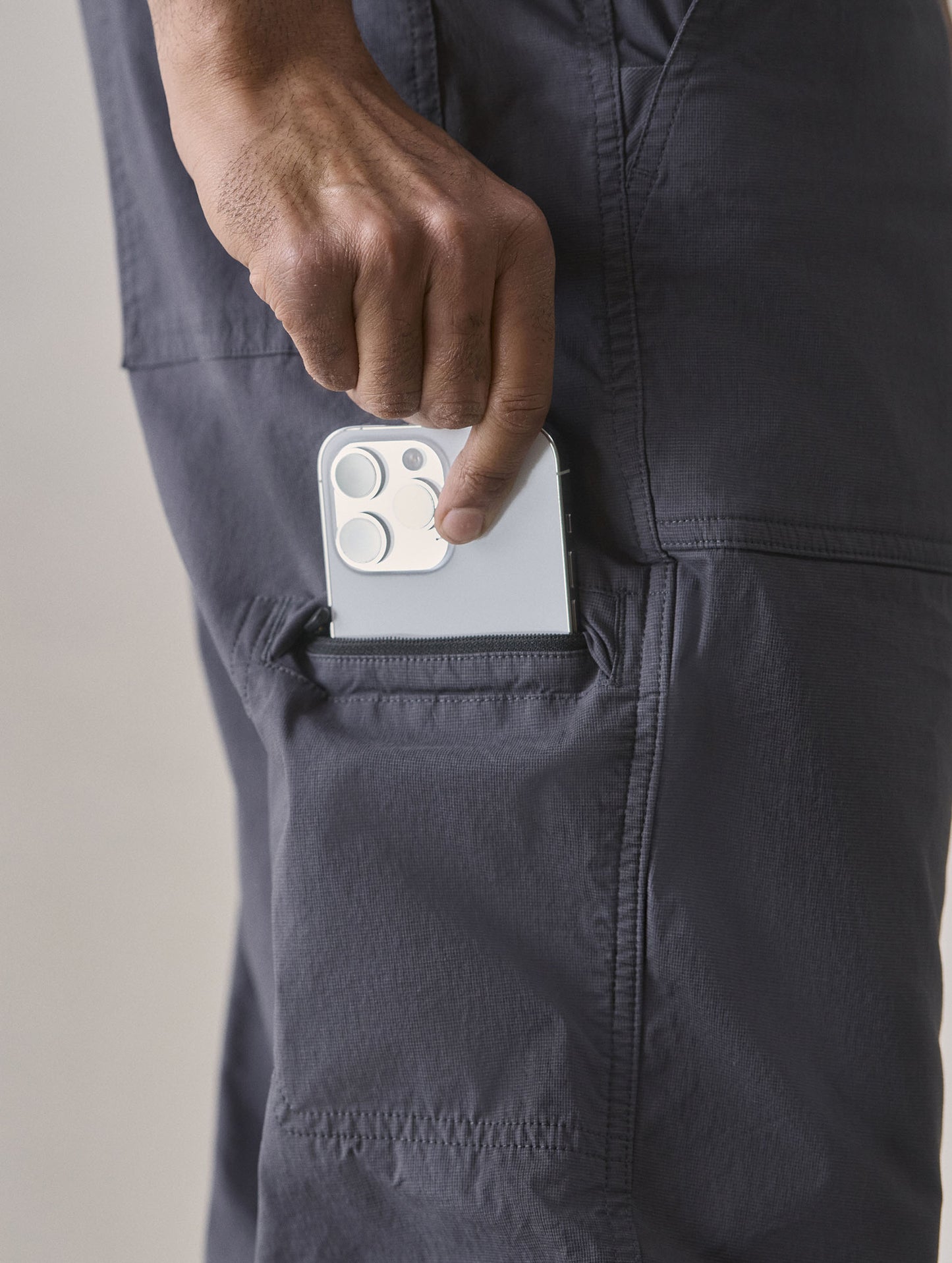Closeup detailed view of man removing iPhone from the dedicated mesh-lined envelope welt smartphone pocket on the Zermatt Hiking Pant in Graphite from AETHER Apparel.