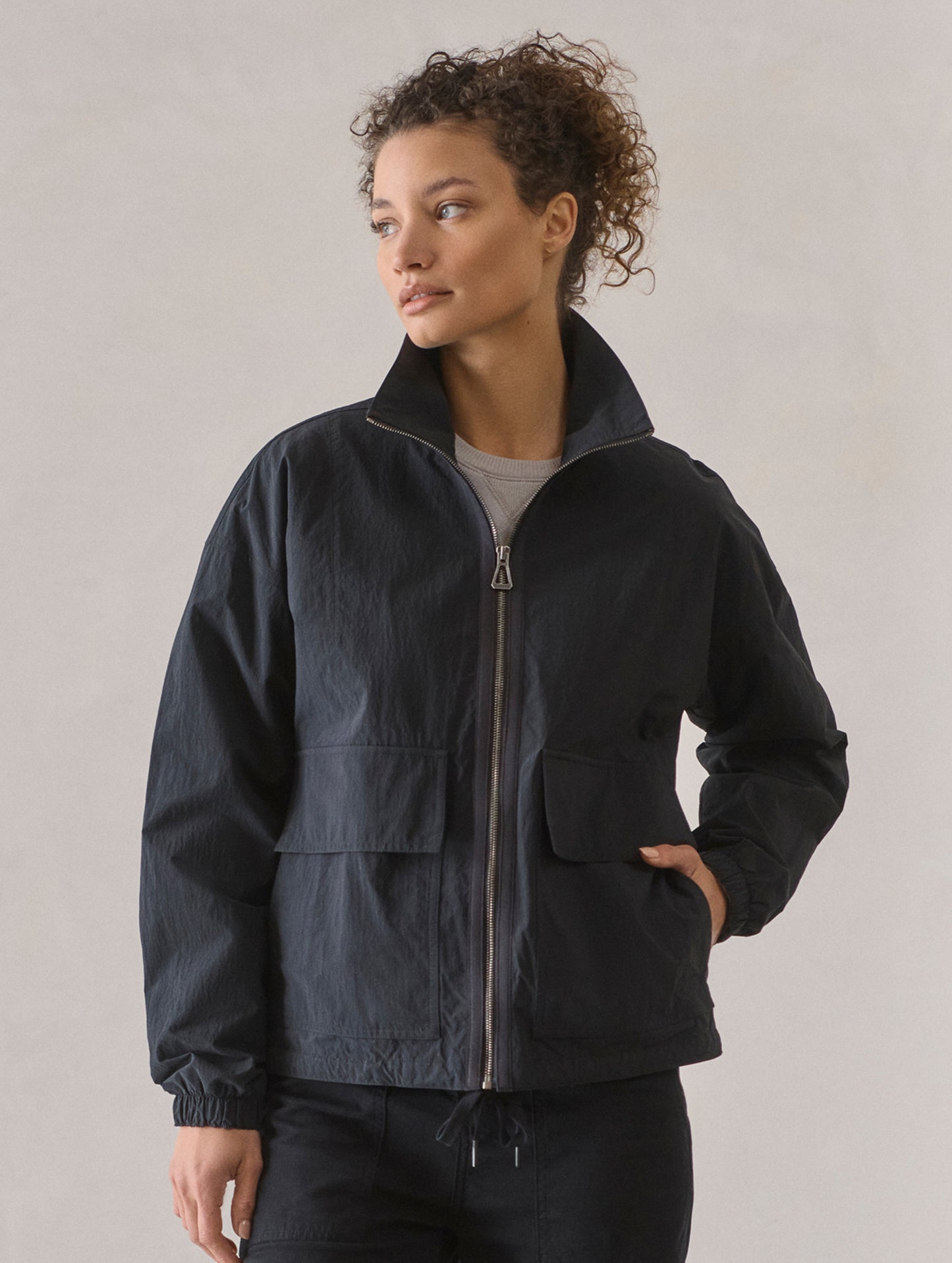 Front upper body view of woman wearing Mila Windbreaker in Onyx Black from AETHER Apparel.