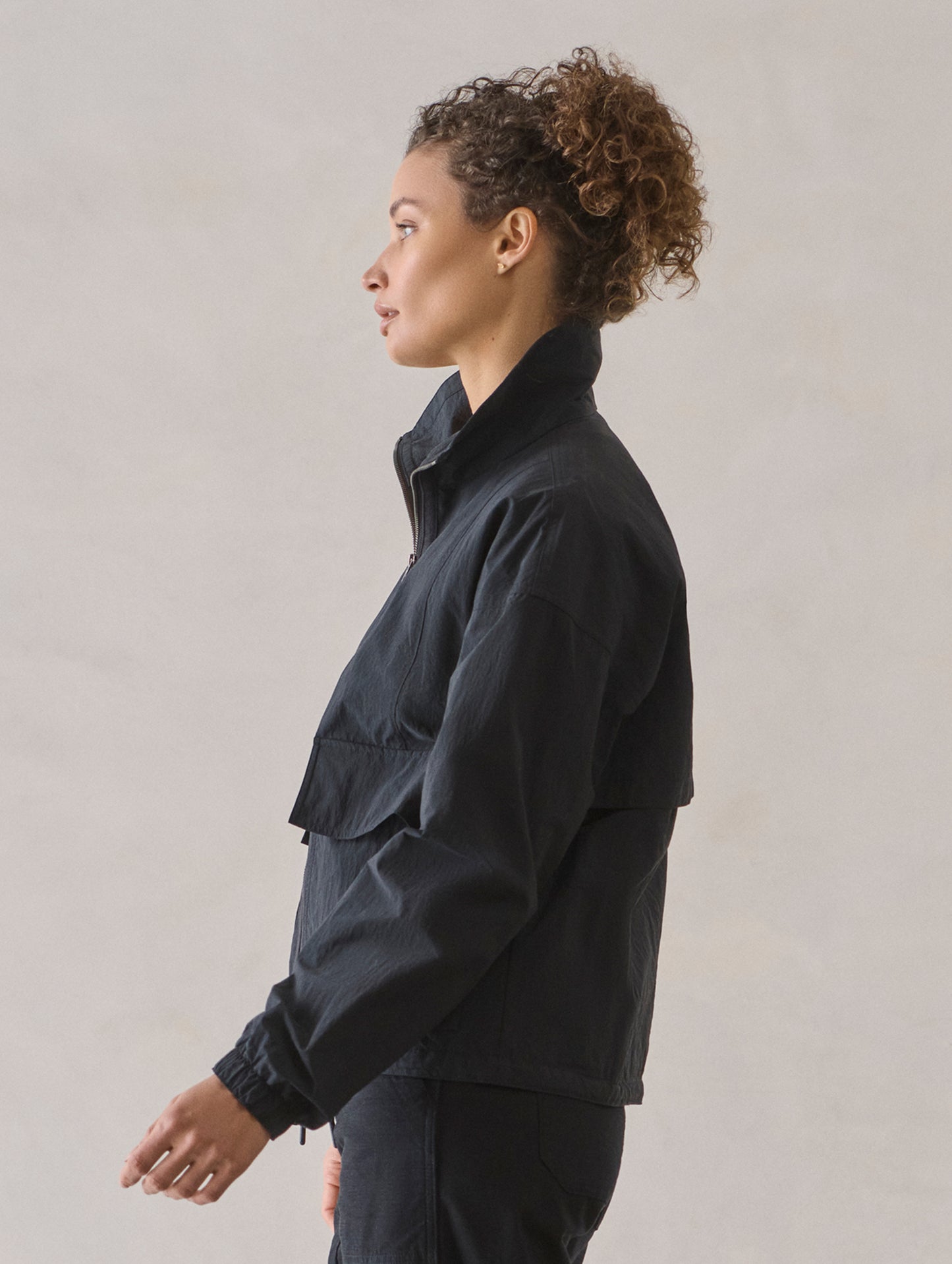 Side profile view of woman wearing Mila Windbreaker in Onyx Black from AETHER Apparel.