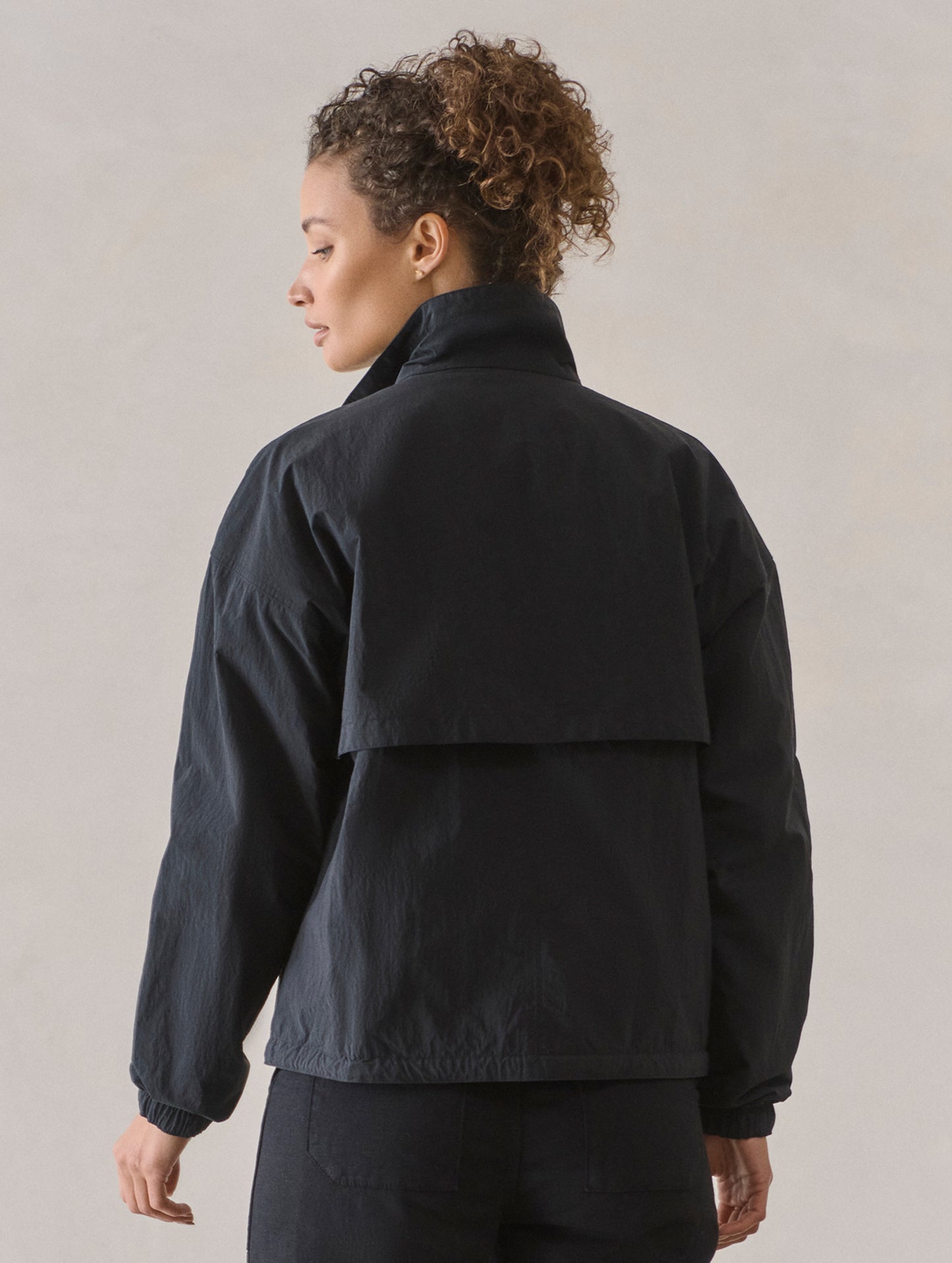 Rear view of woman wearing Mila Windbreaker in Onyx Black from AETHER Apparel.