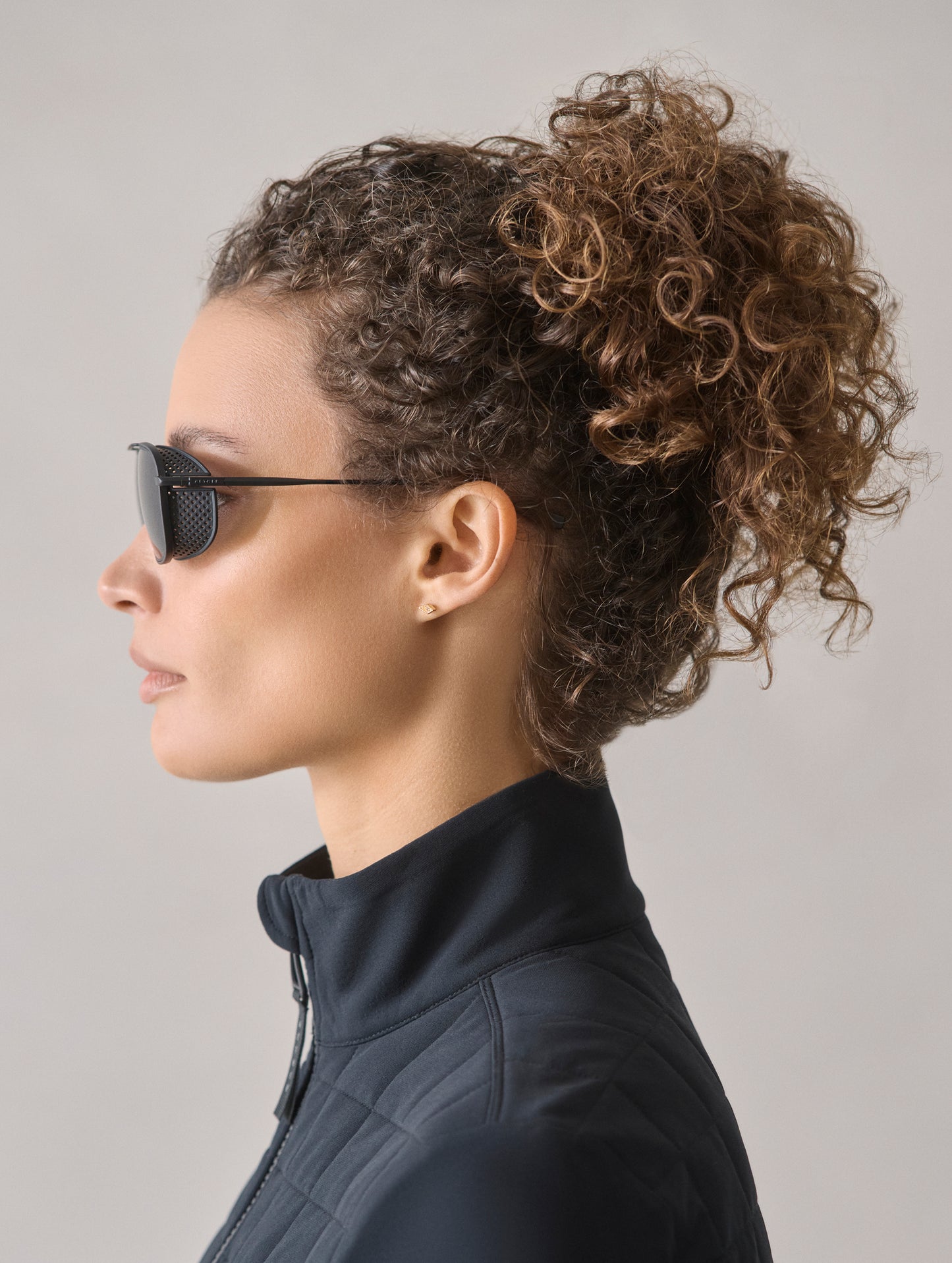 Side profile view of woman wearing Summit Sunglass in Black titanium with black lens from AETHER Apparel.