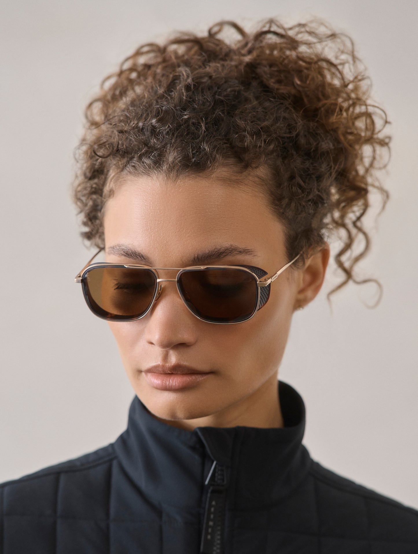 Front 3/4 view of woman wearing Summit Sunglass in Brushed Gold titanium with G15 Lens from AETHER Apparel.