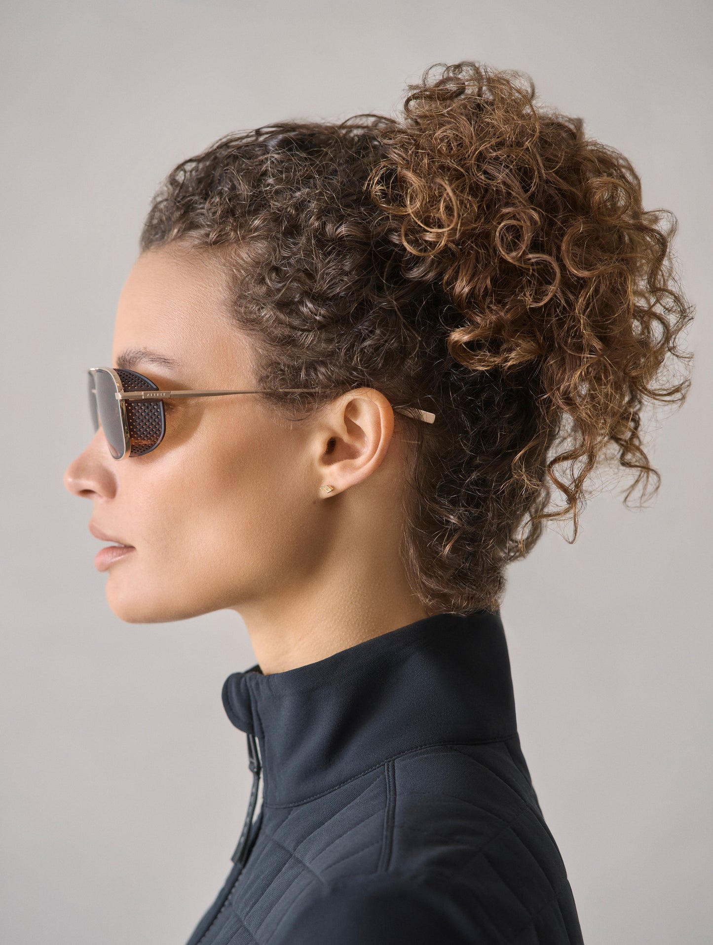 Side profile view of woman wearing Summit Sunglass in Brushed Gold titanium with G15 Lens from AETHER Apparel.