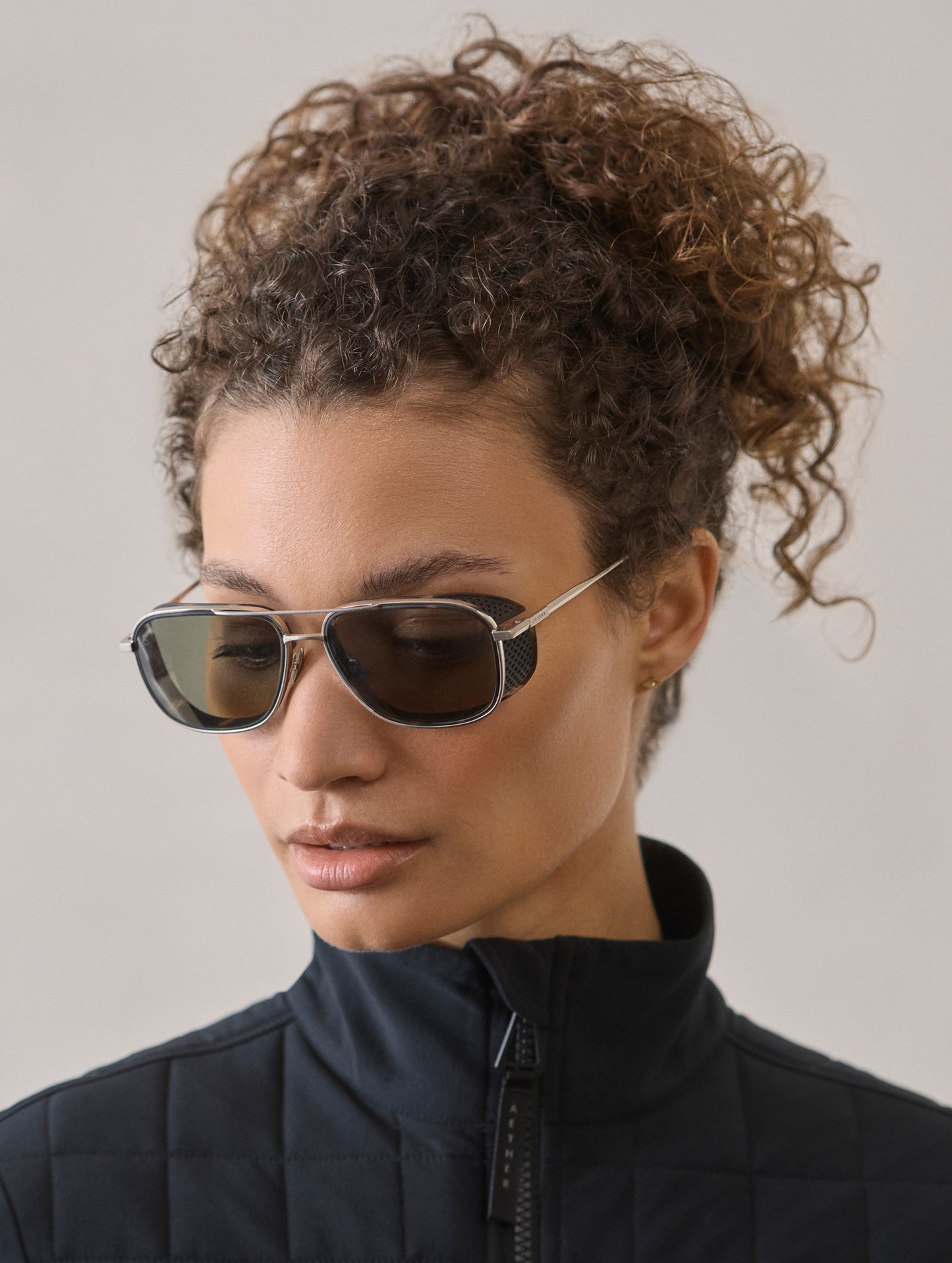 Front 3/4 view of woman wearing Summit Sunglass in Brushed Silver titanium with Grey Lens from AETHER Apparel.