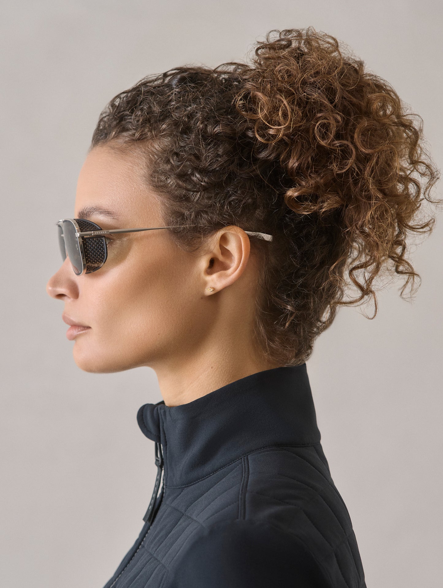 Side profile view of woman wearing Summit Sunglass in Brushed Silver titanium with Grey Lens from AETHER Apparel.