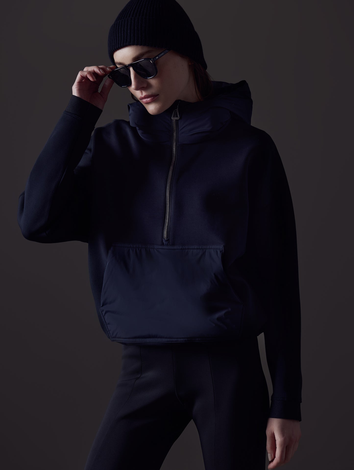 Front angled view of woman with sunglasses and beanie wearing Align Hooded Anorak in Onyx Black from AETHER Apparel.