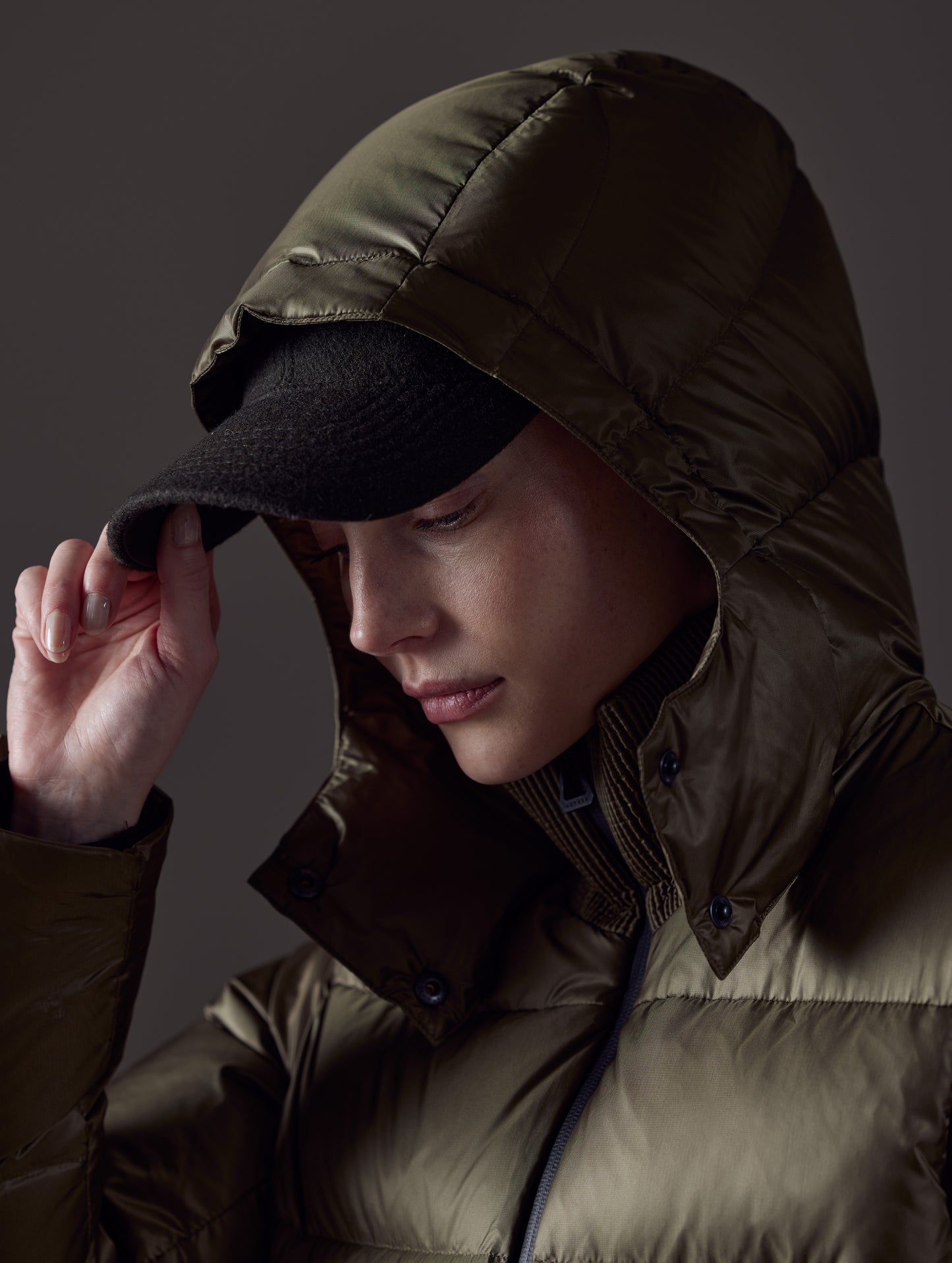 Closeup detailed view of woman with hood up wearing Aura Puffer Jacket in Command Green from AETHER Apparel.