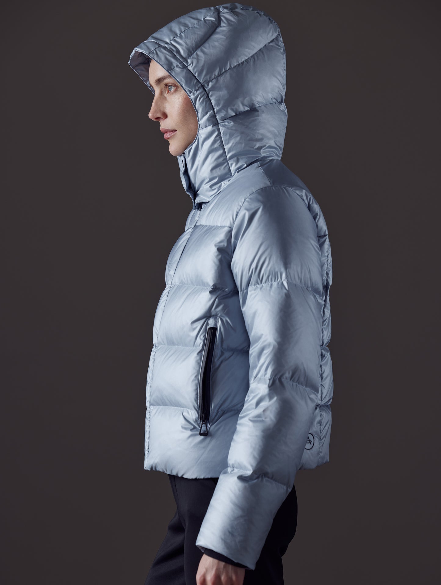 Side profile view of woman with hood up wearing Aura Puffer Jacket in Flight Blue from AETHER Apparel.