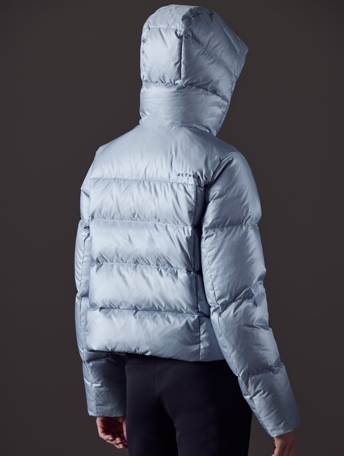 Rear angled view of woman wearing Aura Puffer Jacket in Flight Blue from AETHER Apparel.