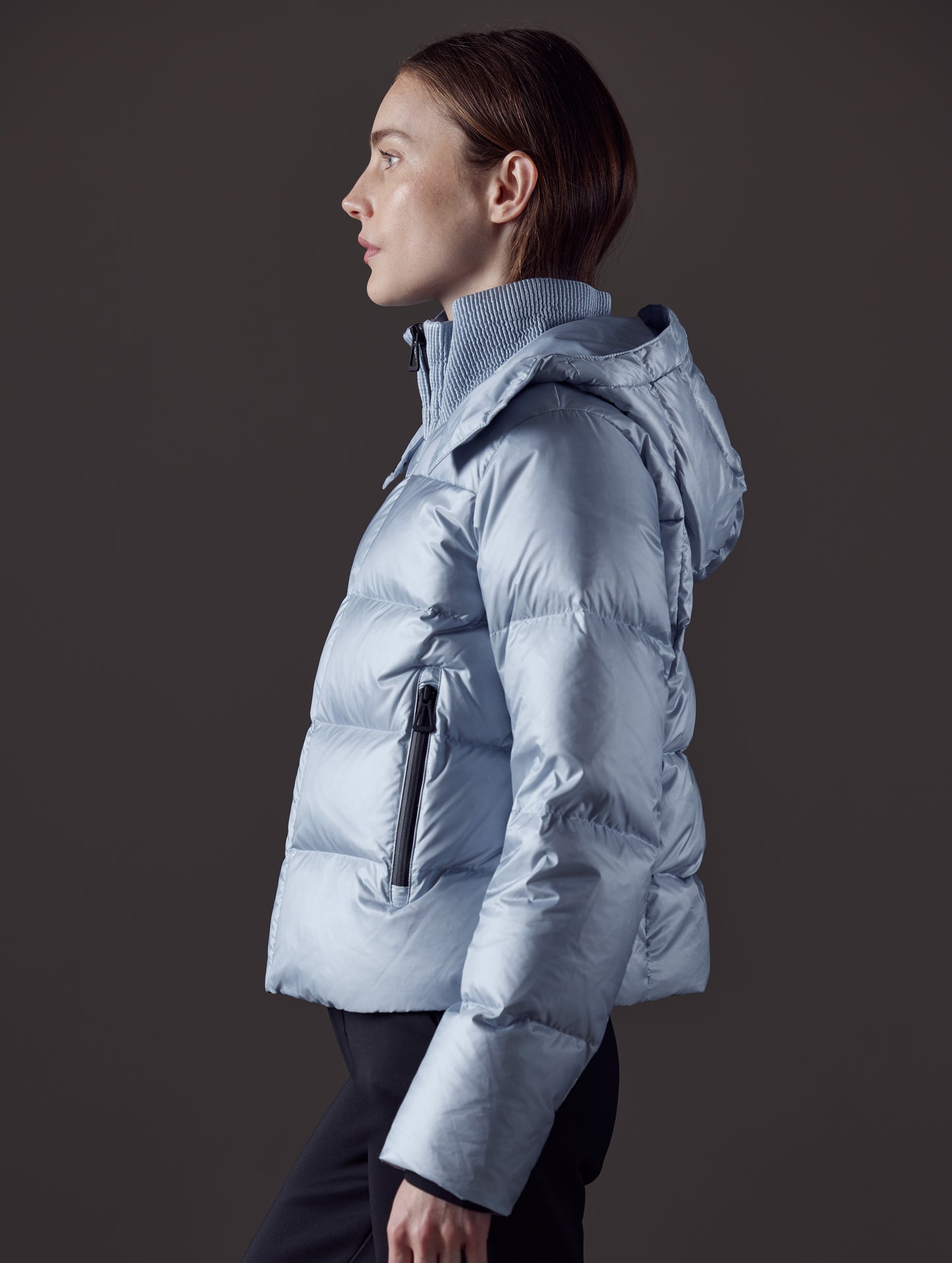 Side profile view of woman with hood down wearing Aura Puffer Jacket in Flight Blue from AETHER Apparel.