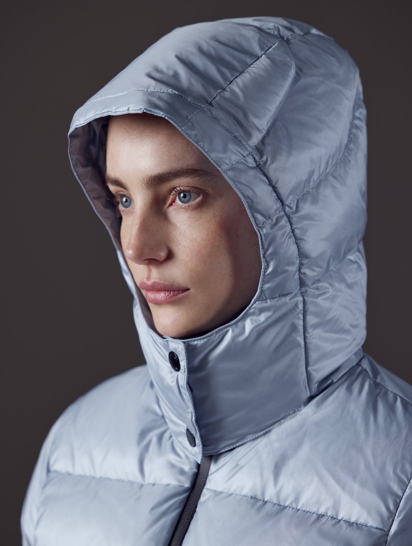 Closeup detailed front angled view of woman with hood up wearing Aura Puffer Jacket in Flight Blue from AETHER Apparel.