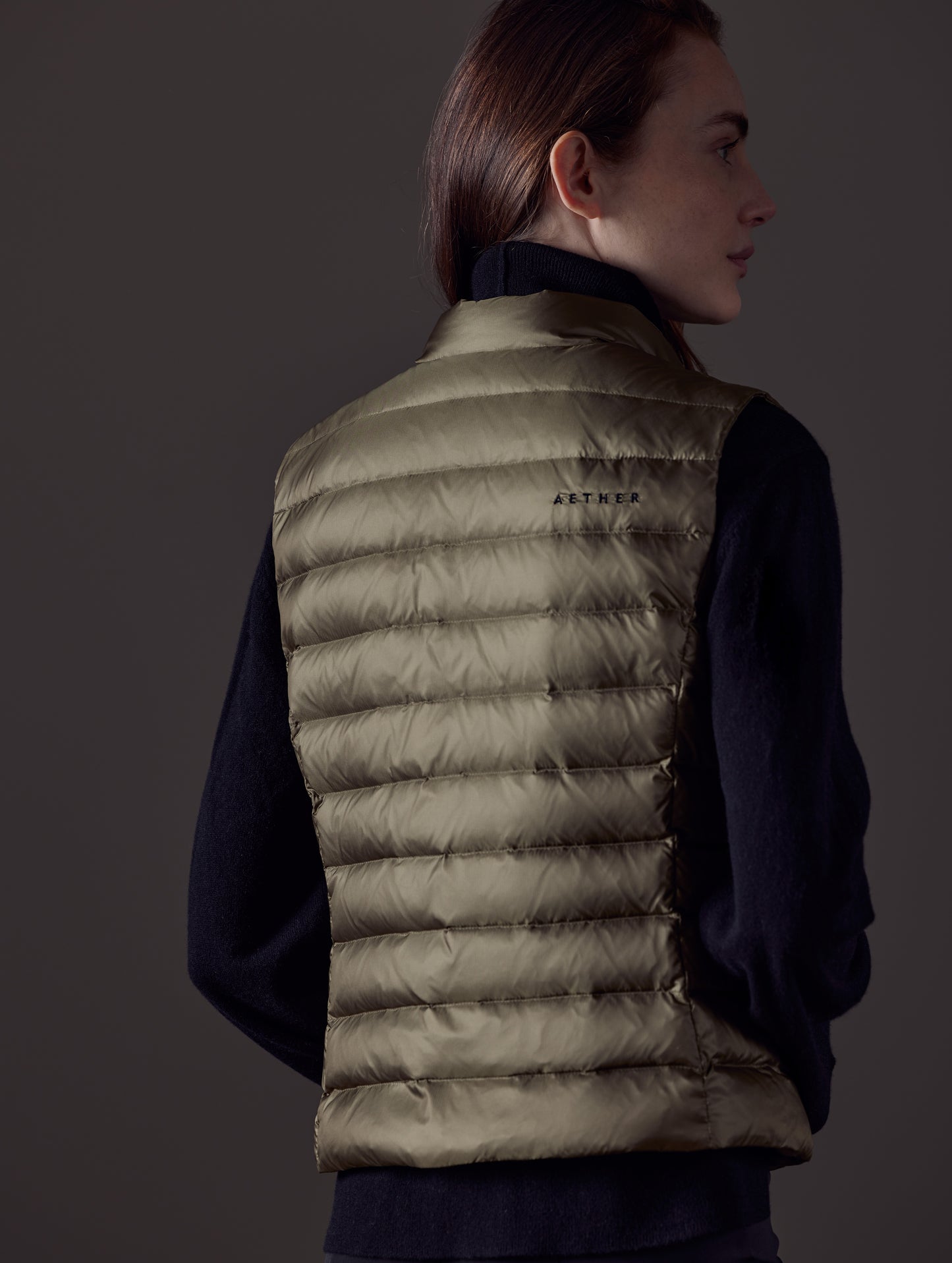 Rear angled view of woman wearing Aura Vest in Command Green from AETHER Apparel.