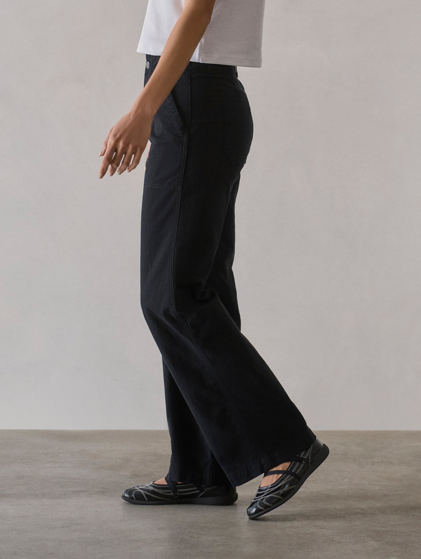 Left side profile lower body view of woman wearing Bella Travel Pant in Onyx Black from AETHER Apparel.