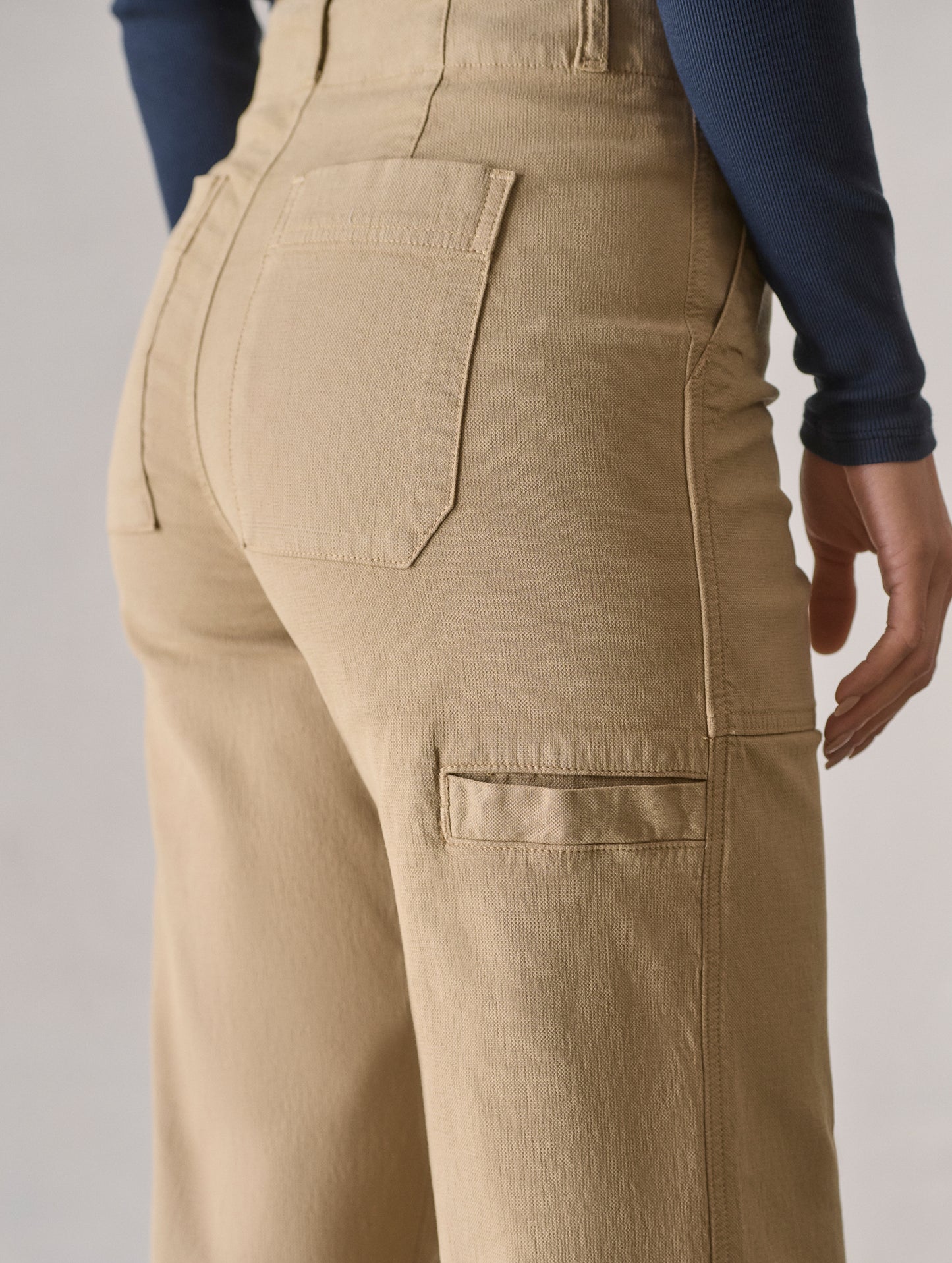 Closeup detailed view of rear patch pocket and welt pocket at the wearer’s left leg on the Bella Travel Pant in Desert Tan from AETHER Apparel.