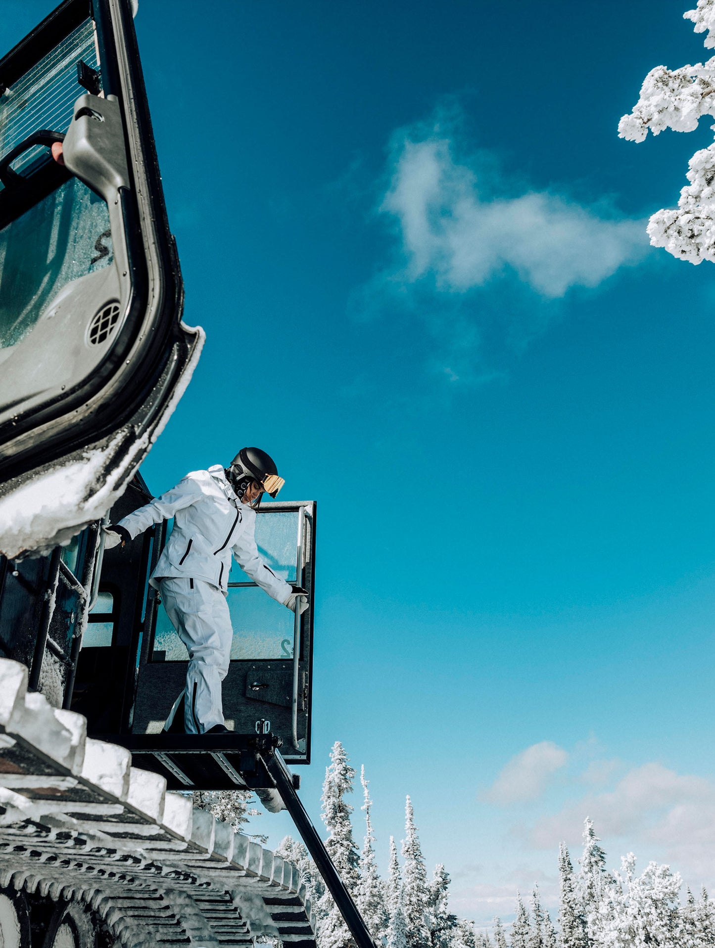 Outdoor lifestyle view of woman climbing off of snow track vehicle wearing the Boyd Snow Pant and Boyd Snow Jacket in White from AETHER Apparel.
