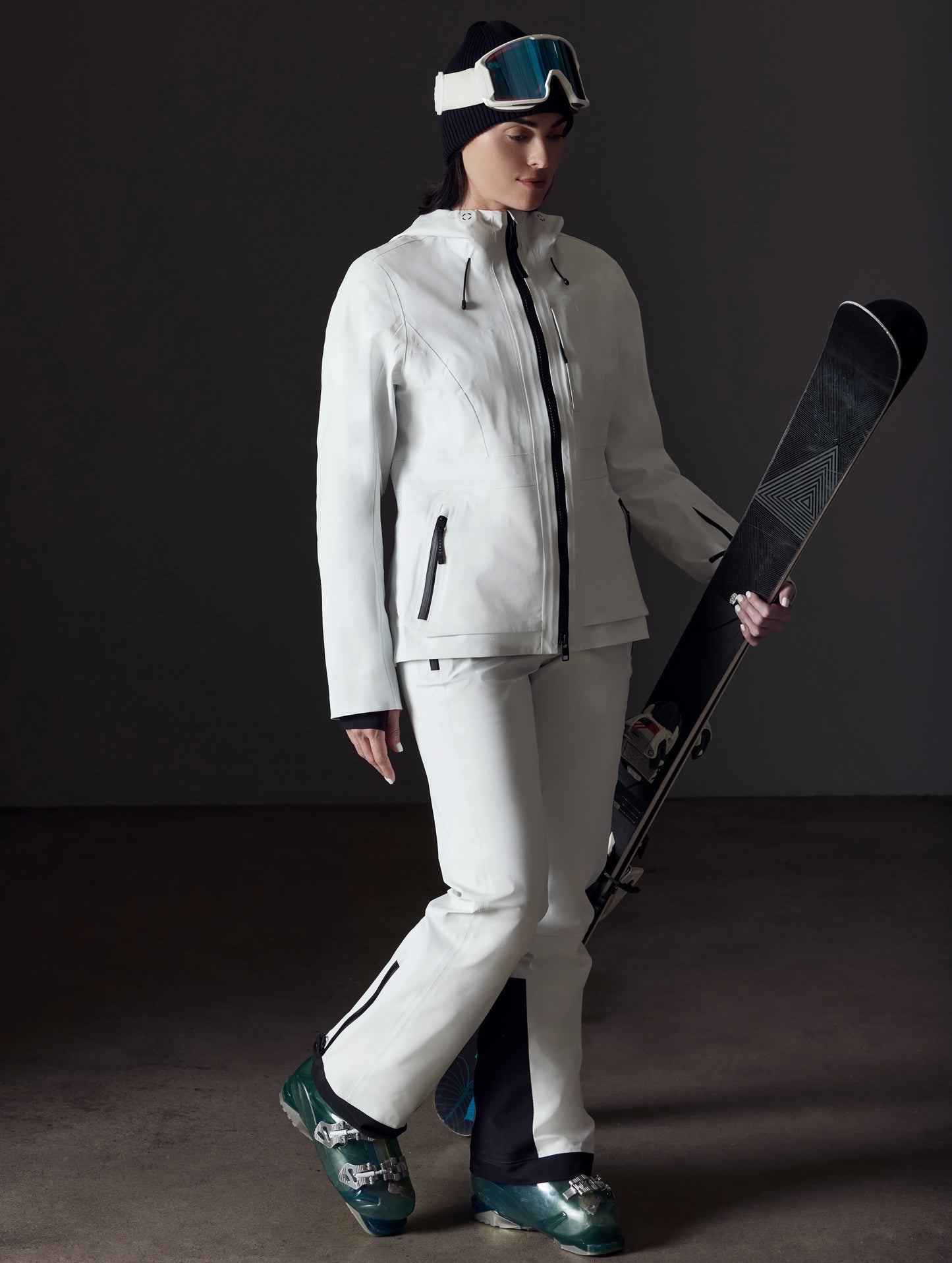Front angled full-body view of woman holding skis wearing Boyd Snow Jacket in White from AETHER Apparel.