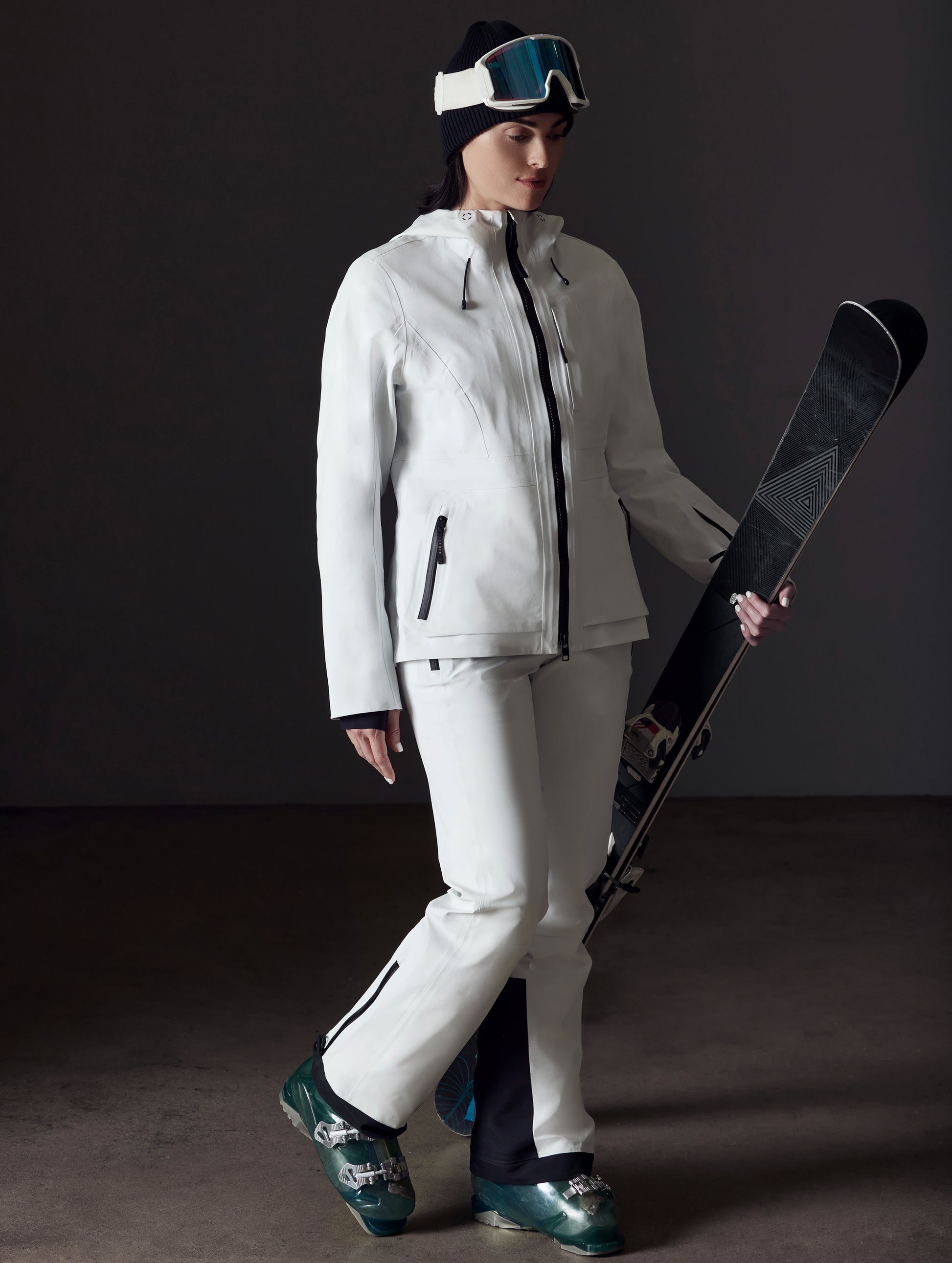 Front angled full-body view of woman holding skis wearing Boyd Snow Jacket in White from AETHER Apparel.