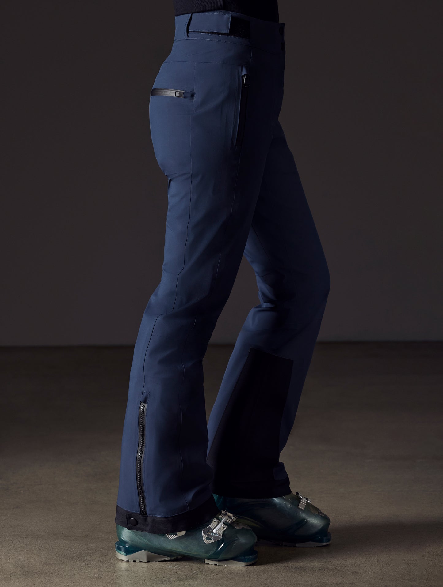 Side profile lower body view of woman wearing Boyd Snow Pant in Total Eclipse dark blue from AETHER Apparel.