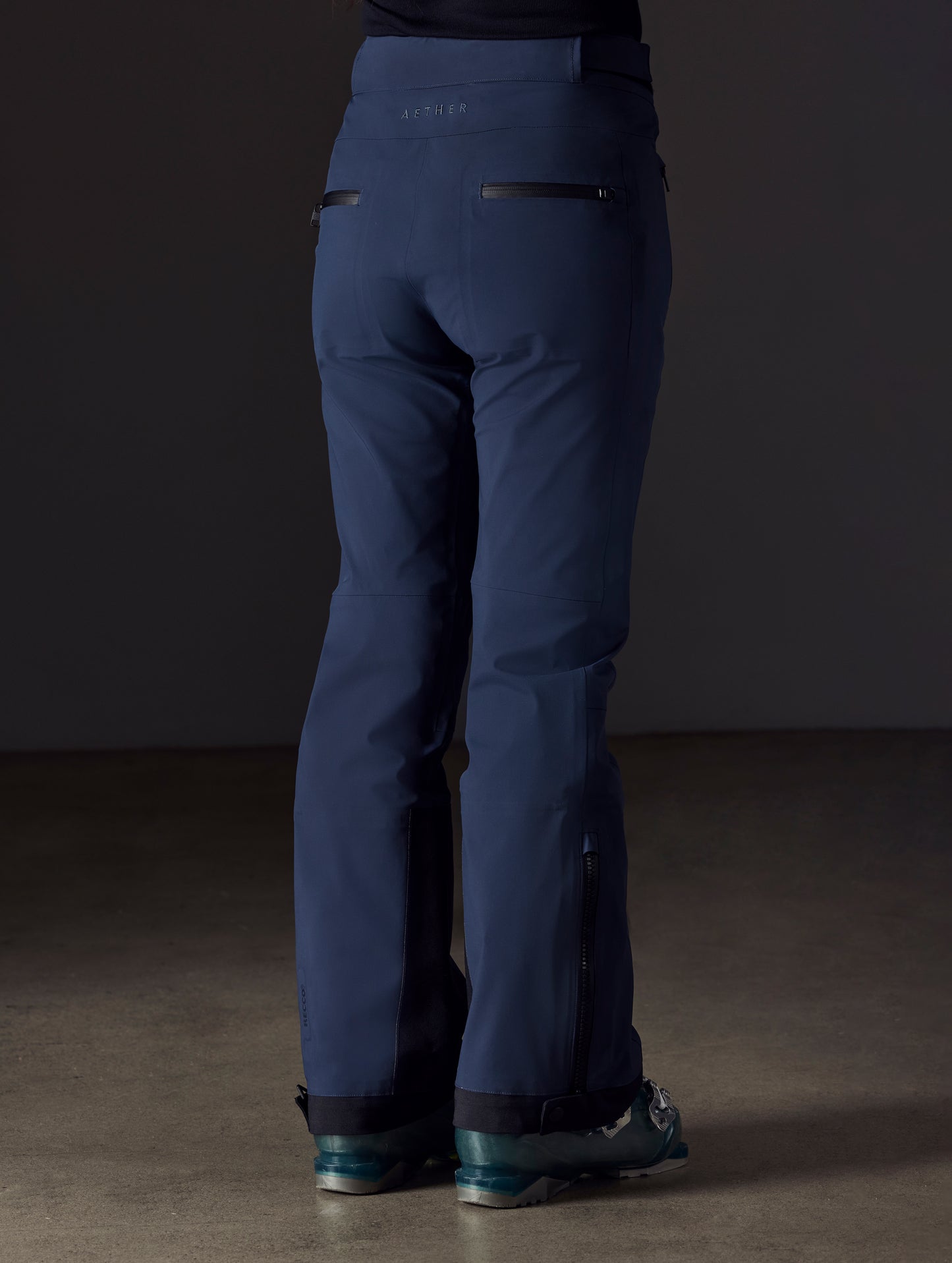 Rear angled lower body view of woman wearing Boyd Snow Pant in Total Eclipse dark blue from AETHER Apparel.