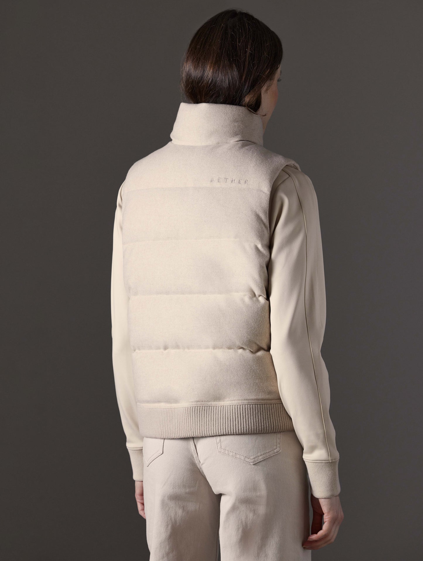 Rear angled view of woman wearing Channing Vest 2.0 in Bone Heather from AETHER Apparel.