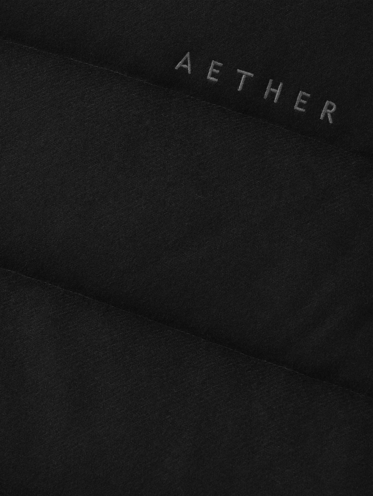 Closeup detailed view of the embroidered AETHER wordmark on the Channing Vest 2.0 in Onyx Black from AETHER Apparel.