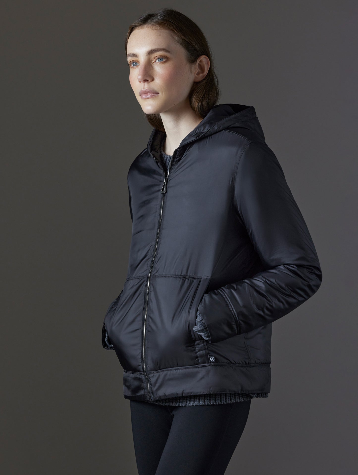 Front angled view of woman with hands in pockets wearing Eco Space Hoodie in Onyx Black from AETHER Apparel.
