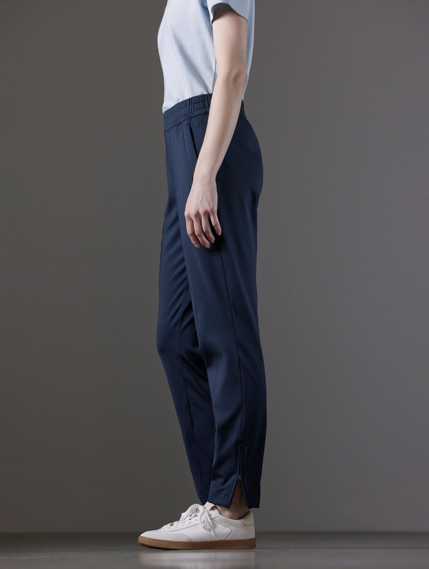 Side profile lower body view of woman wearing Eloise Travel Slim Pant in Total Eclipse dark blue from AETHER Apparel.