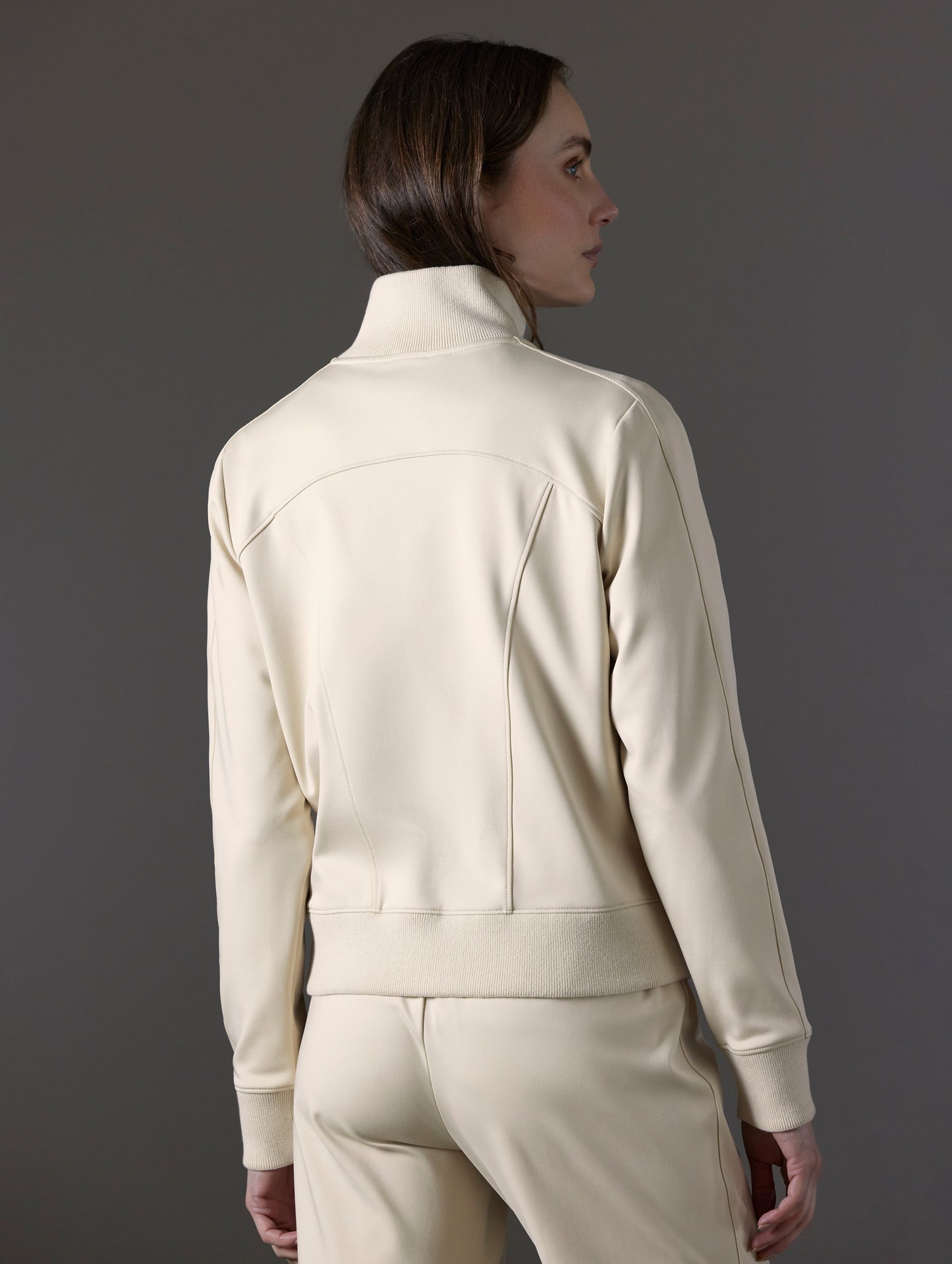 Rear angled view of woman wearing Eloise Travel Jacket in Bone white from AETHER Apparel.