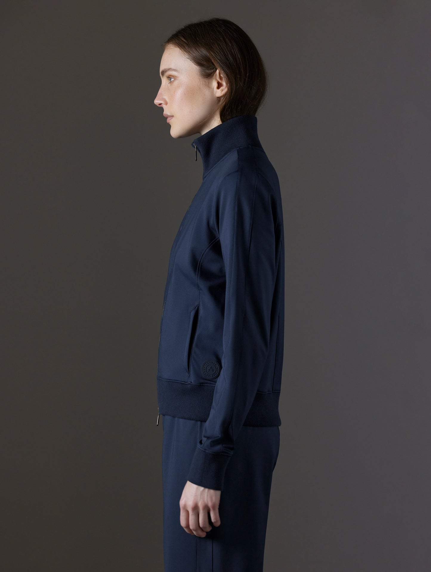 Side profile view of woman wearing Eloise Travel Jacket in Total Eclipse dark blue from AETHER Apparel.