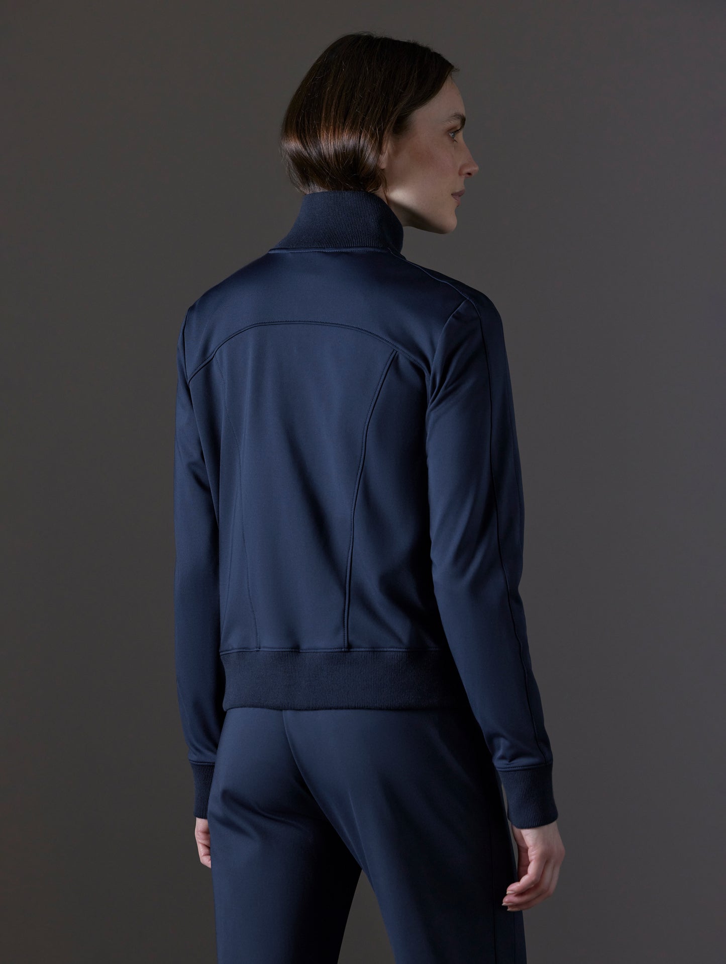 Rear angled view of woman wearing Eloise Travel Jacket in Total Eclipse dark blue from AETHER Apparel.