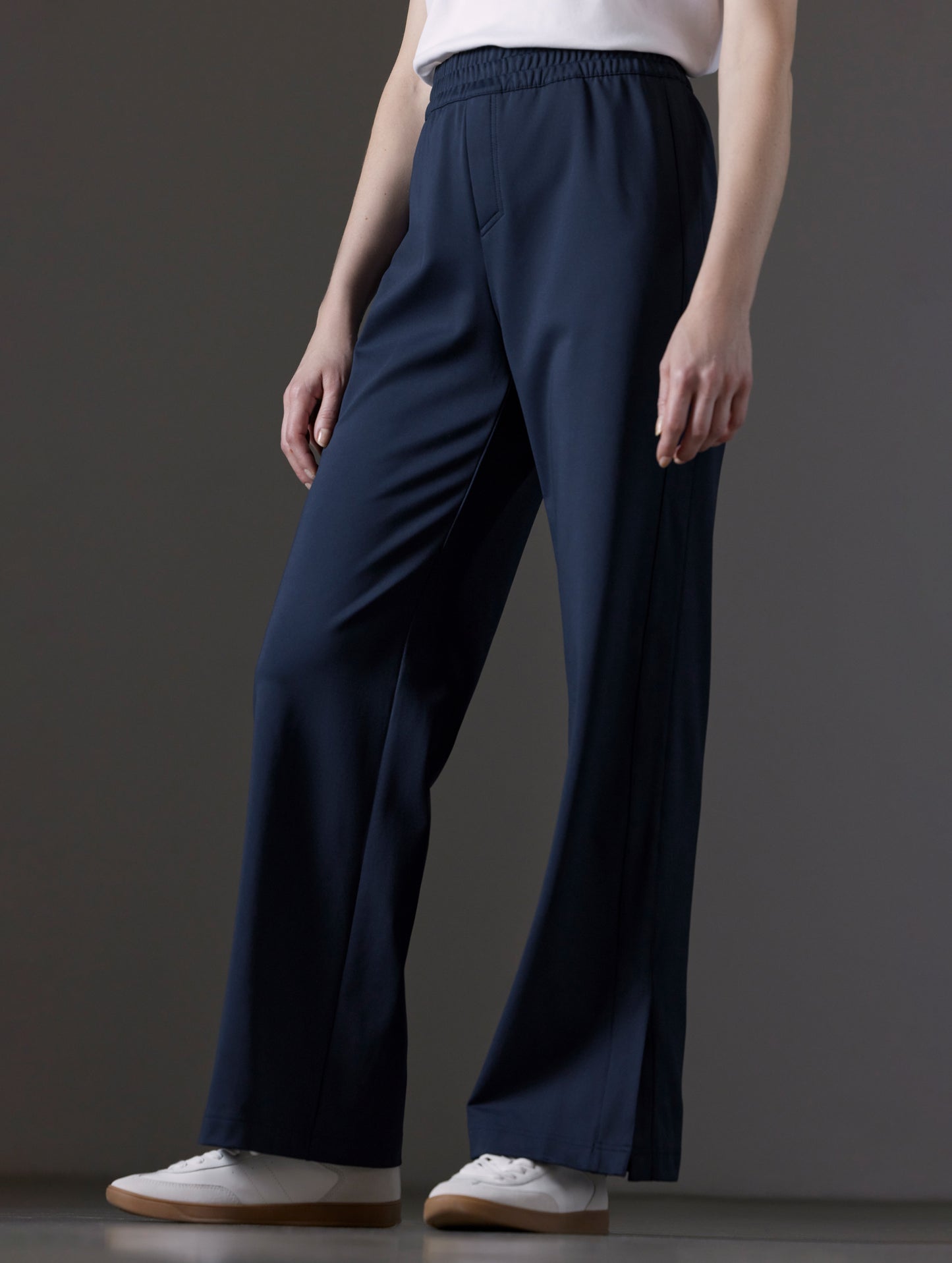 Front angled lower body view of woman wearing Eloise Travel Slim Pant in Total Eclipse dark blue from AETHER Apparel.