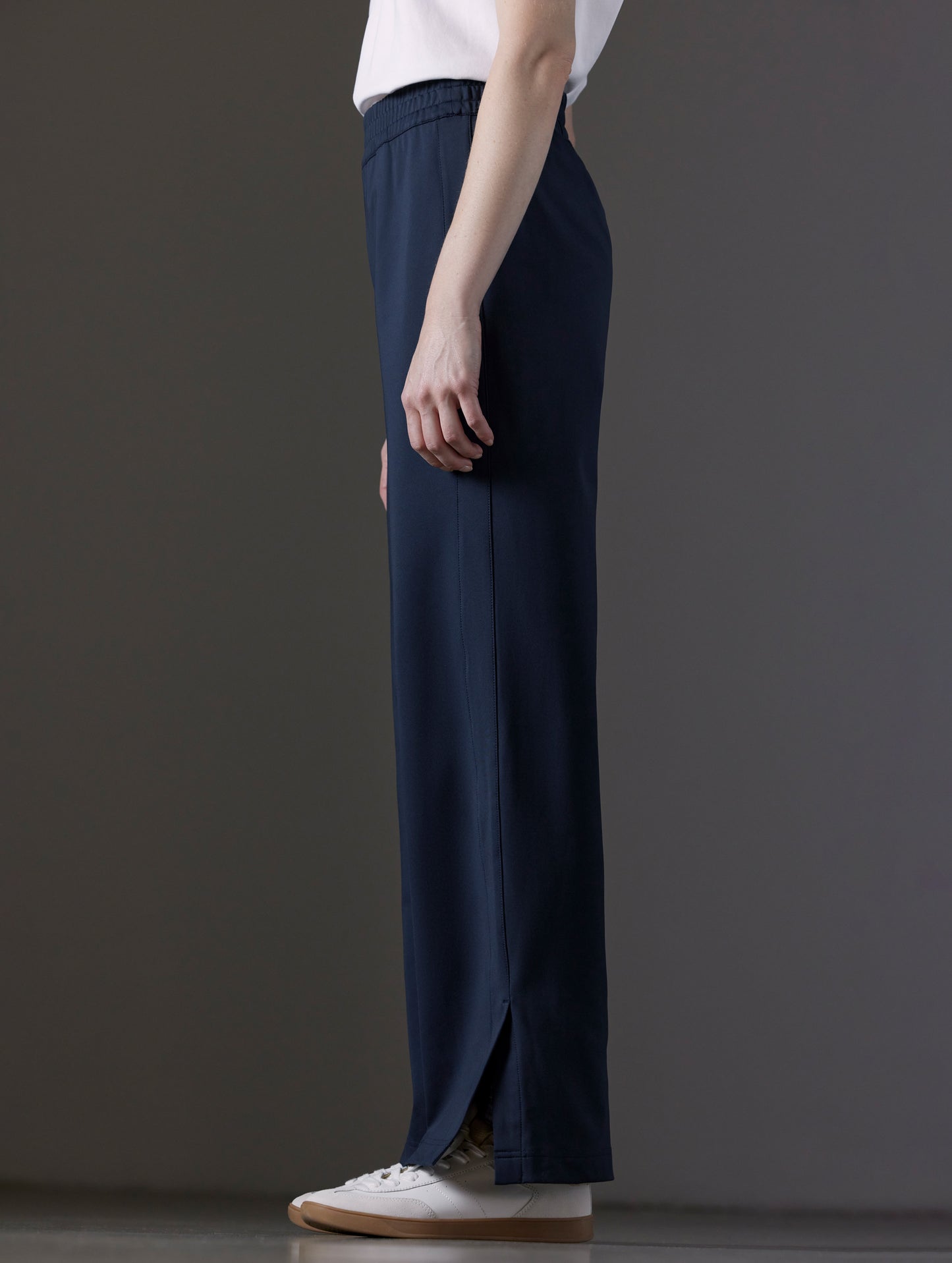 Side profile lower body view of woman wearing Eloise Travel Slim Pant in Total Eclipse dark blue from AETHER Apparel.