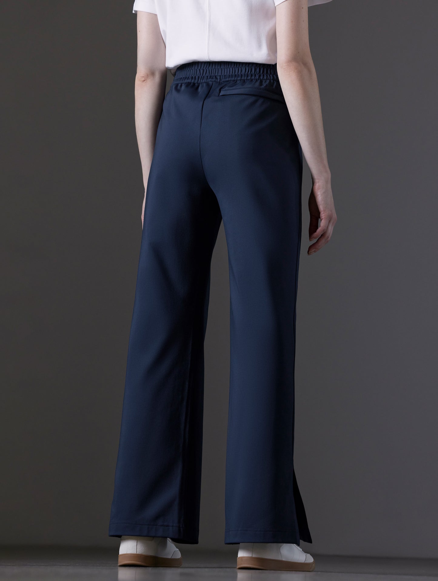 Rear angled lower body view of woman wearing Eloise Travel Slim Pant in Total Eclipse dark blue from AETHER Apparel.
