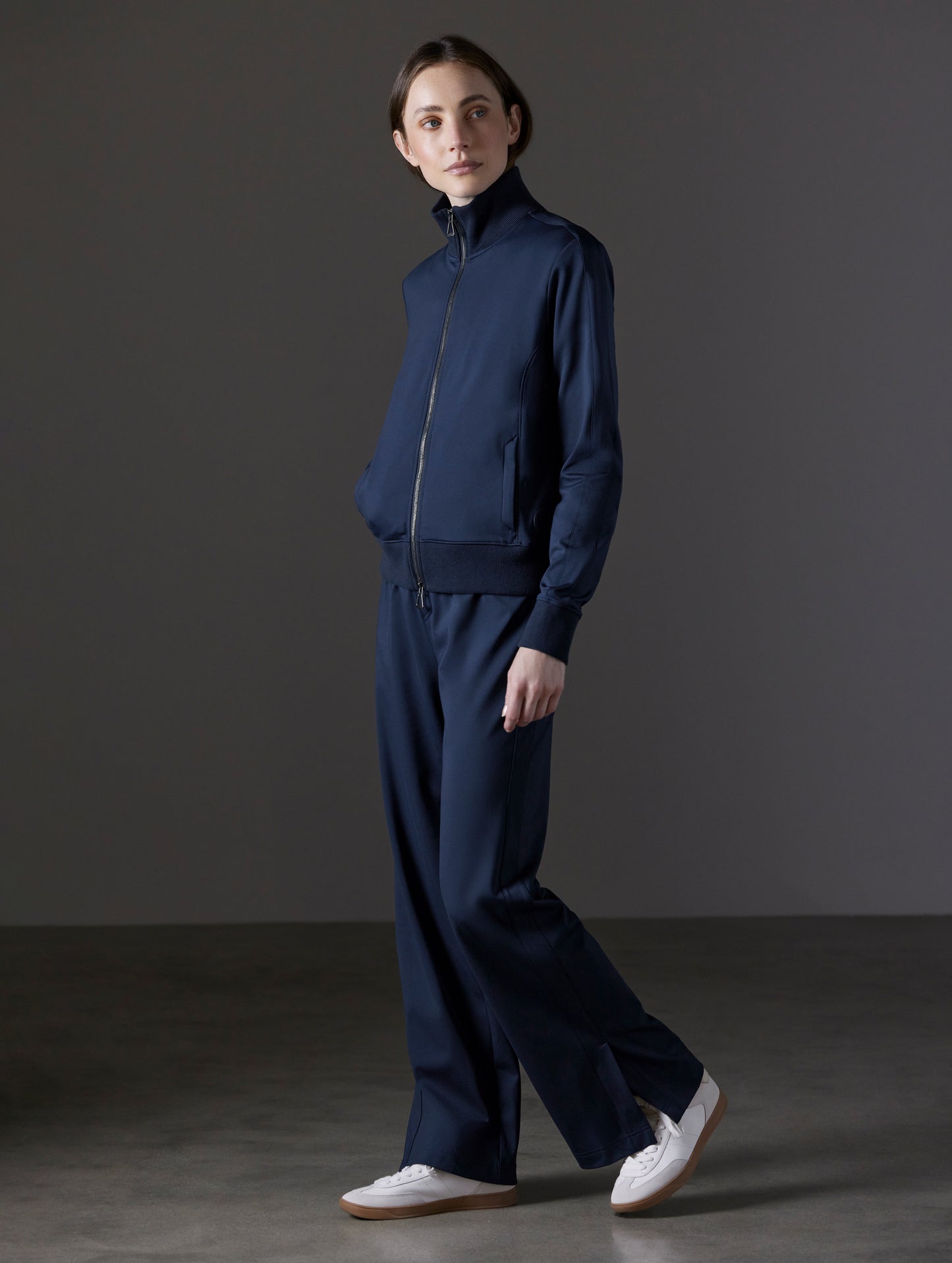 Front angled full-body view of woman wearing Eloise Travel Slim Pant in Total Eclipse dark blue from AETHER Apparel.