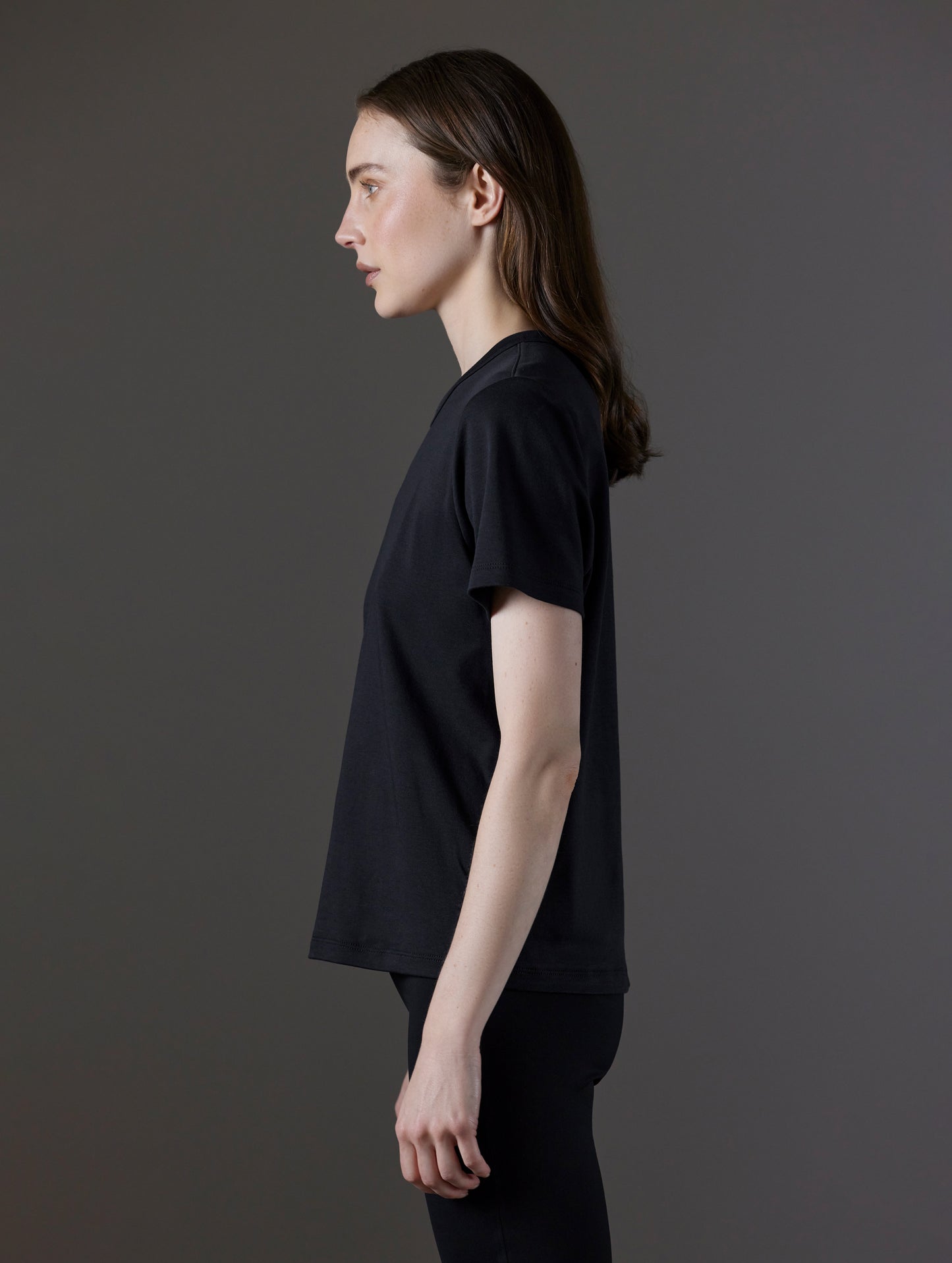 Side profile view of woman wearing Emery Pima Tee in Onyx Black from AETHER Apparel.