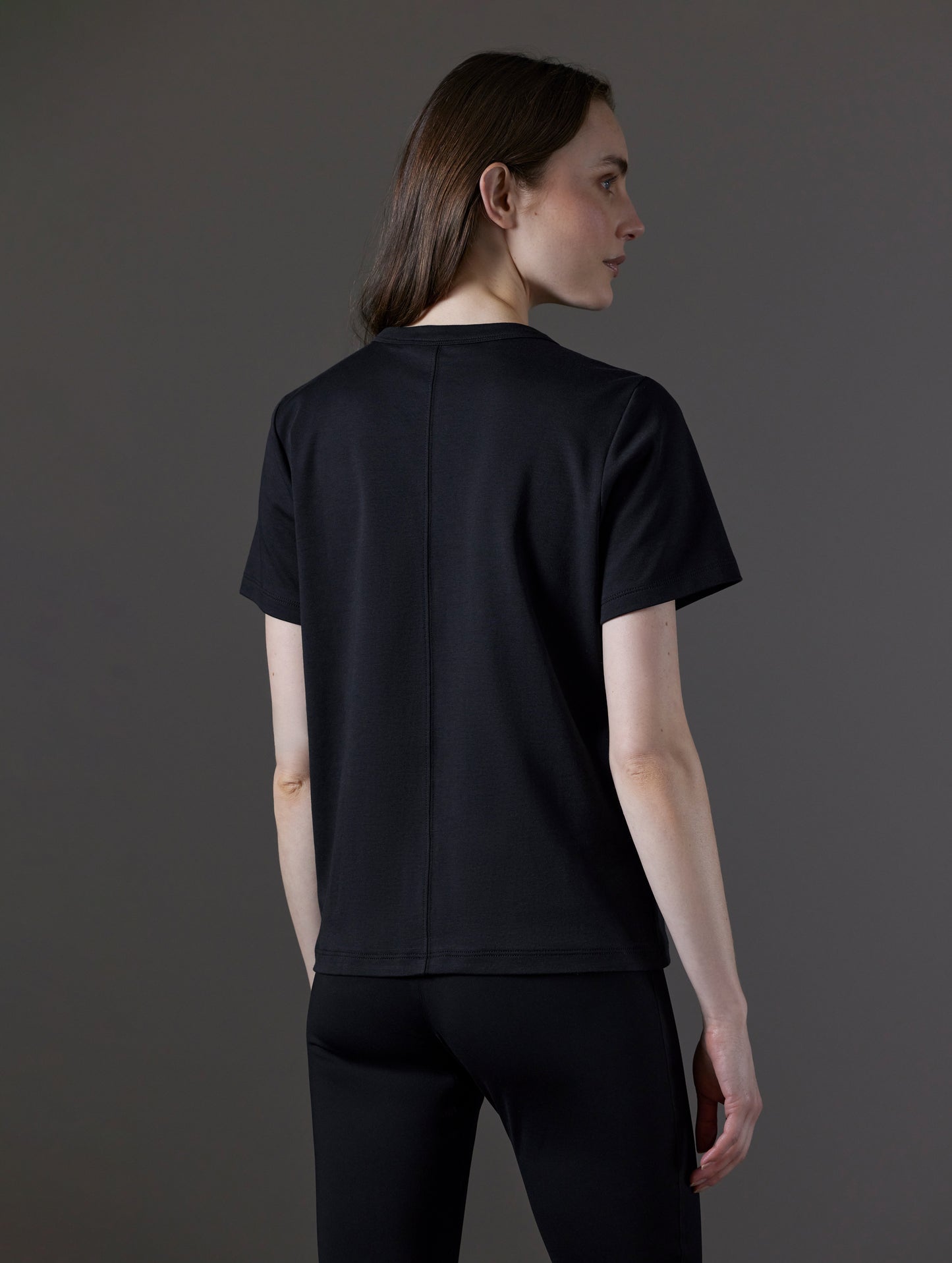 Rear angled view of woman wearing Emery Pima Tee in Onyx Black from AETHER Apparel.