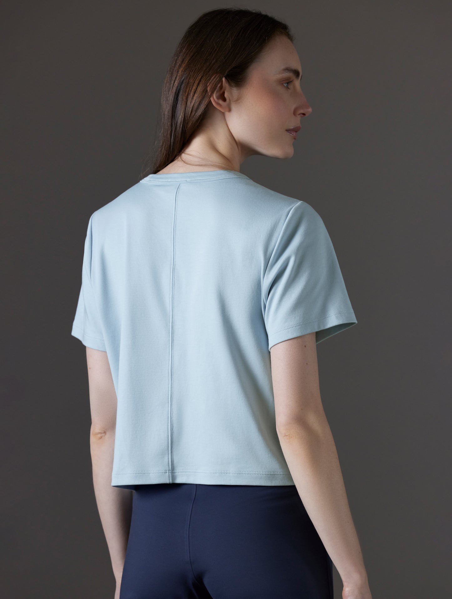 Rear angled view of woman wearing Emery Pima Cropped Tee in Flight Blue from AETHER Apparel.