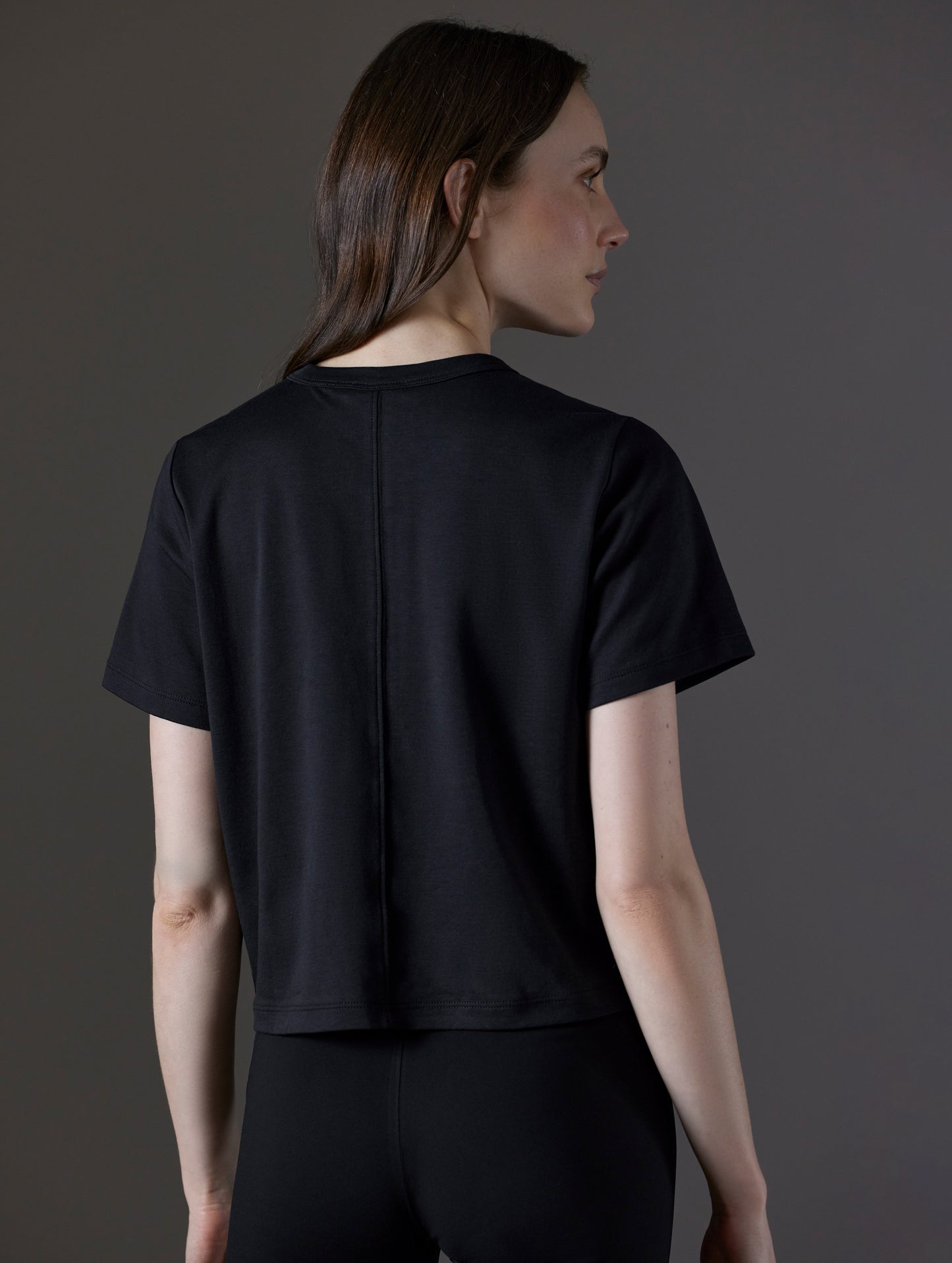 Rear angled view of woman wearing Emery Pima Cropped Tee in Onyx Black from AETHER Apparel.