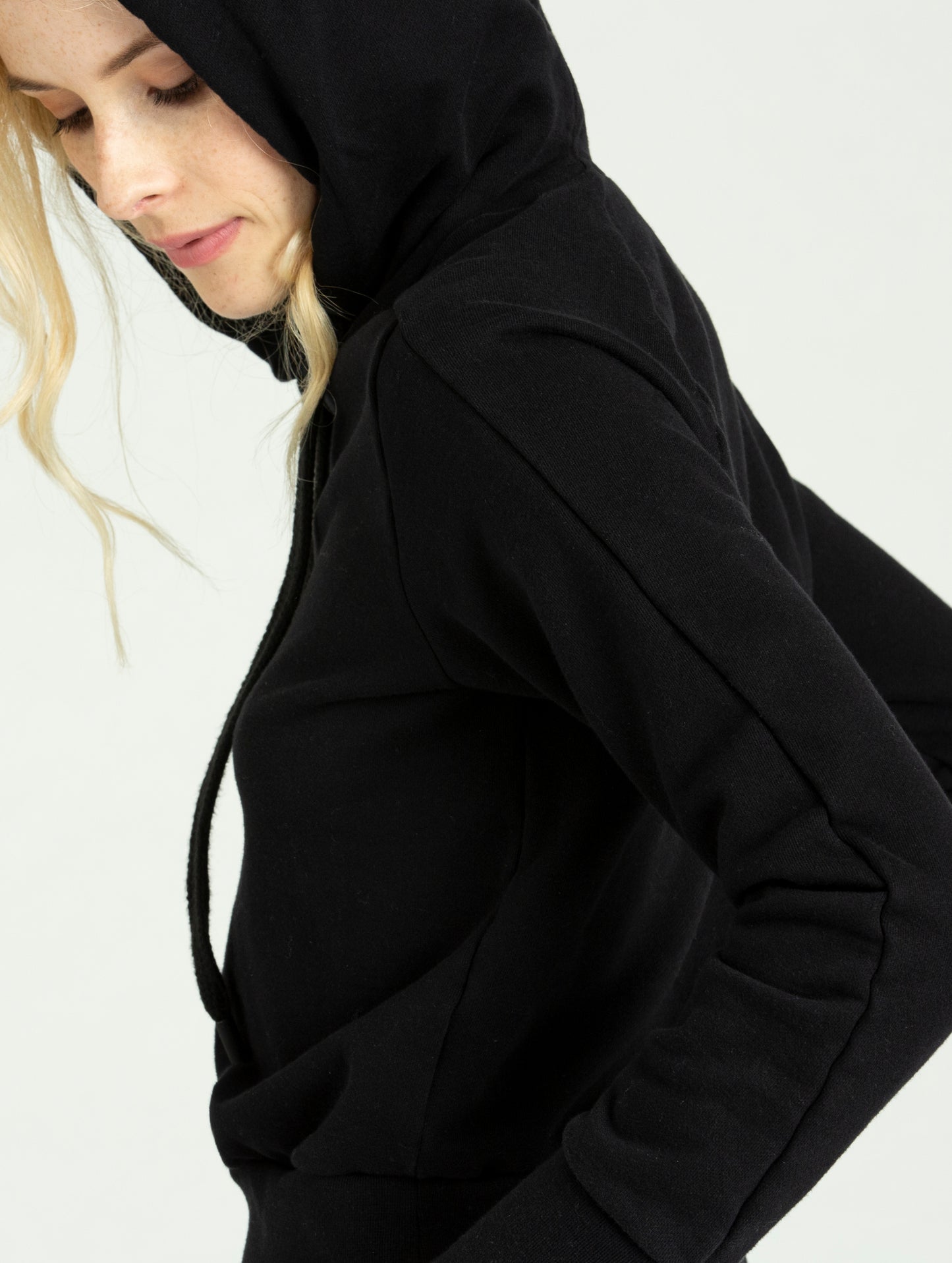 Side view of woman wearing black Journey Pullover with hood from AETHER Apparel.