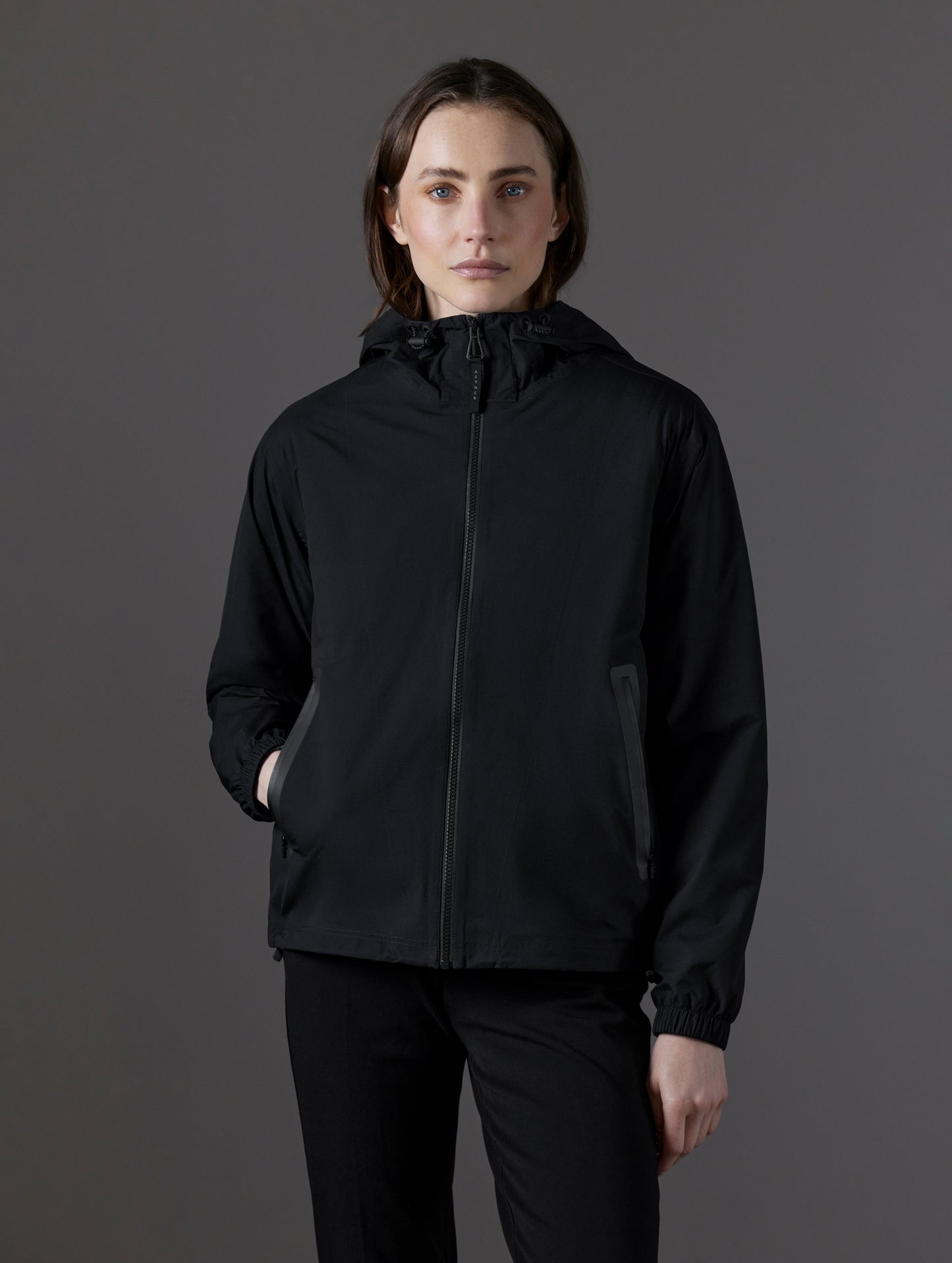 Front body view of woman with hand in pocket wearing Kite Lightweight Jacket in Onyx Black from AETHER Apparel.