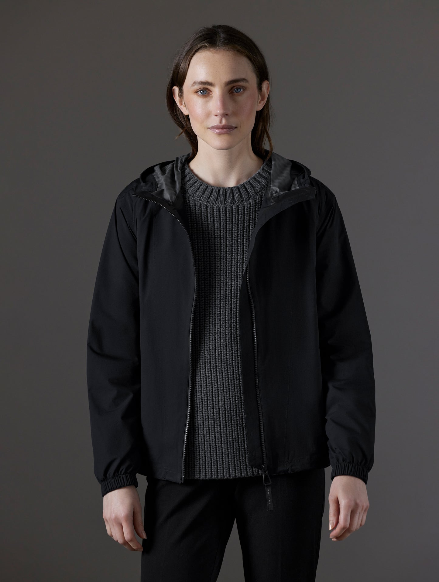 Front body view of woman wearing unzipped Kite Lightweight Jacket in Onyx Black from AETHER Apparel.
