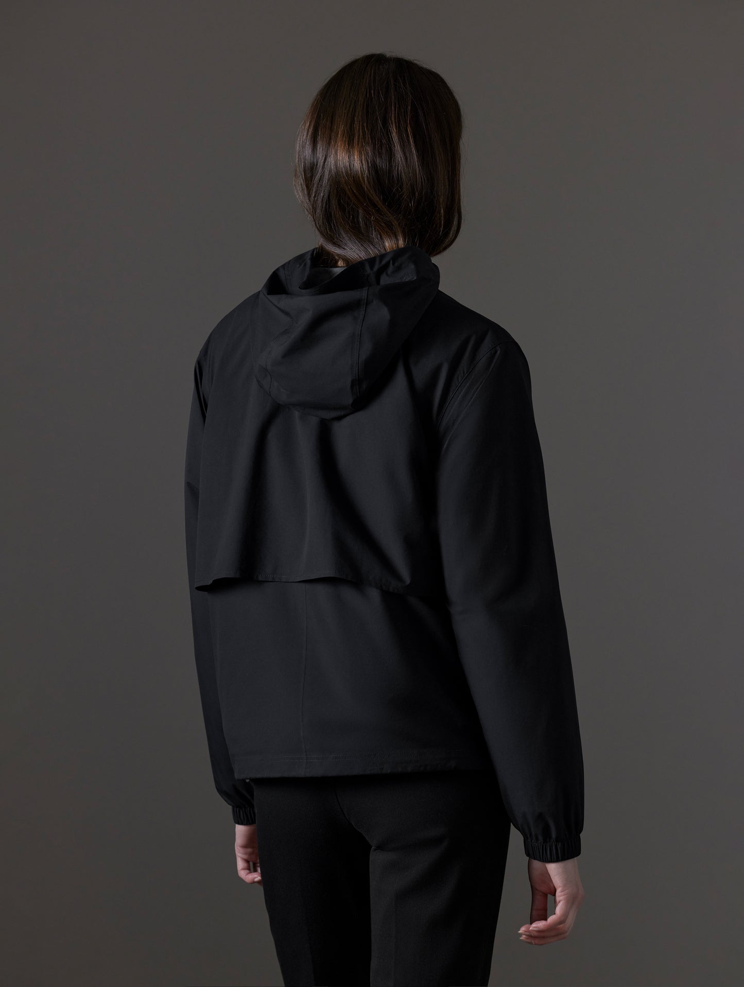 Rear angled view of woman wearing Kite Lightweight Jacket in Onyx Black from AETHER Apparel.