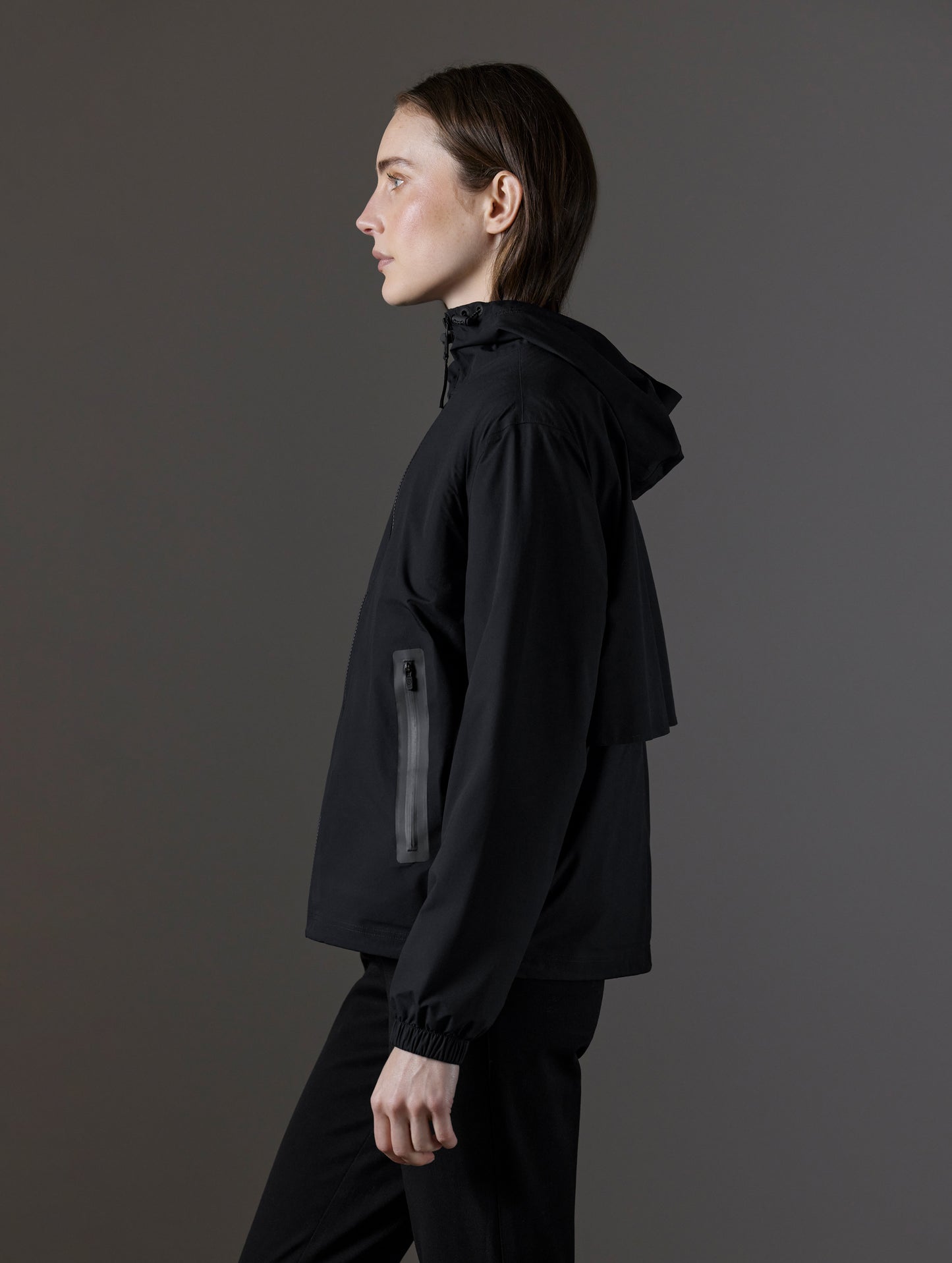 Side profile view of woman wearing Kite Lightweight Jacket in Onyx Black from AETHER Apparel.