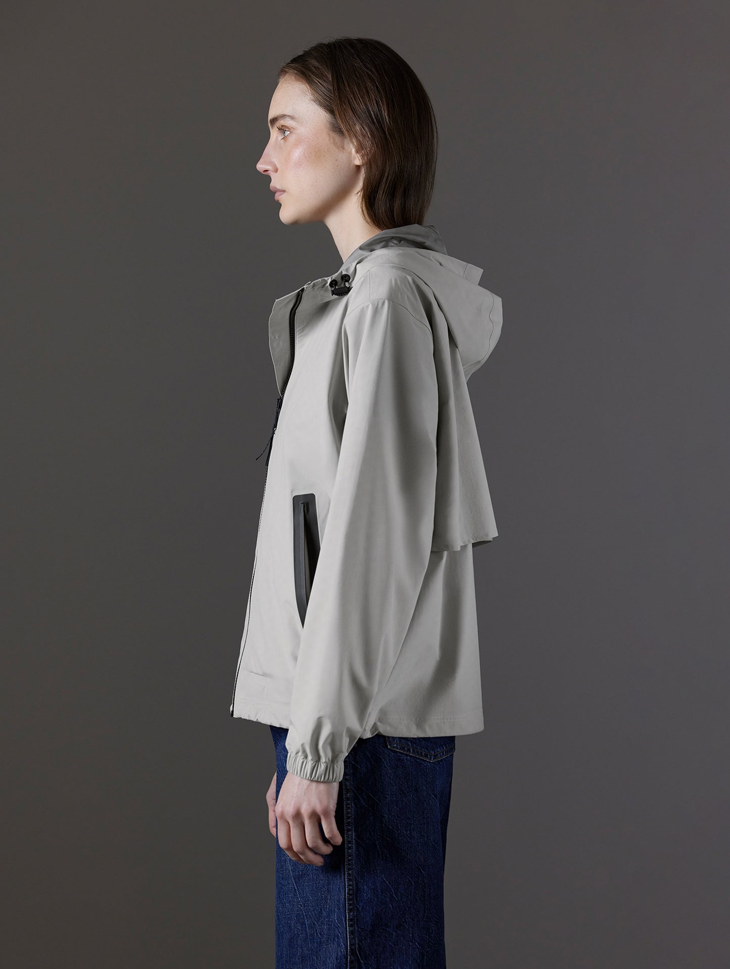 Side profile view of woman wearing Kite Lightweight Jacket in Stone Grey from AETHER Apparel.