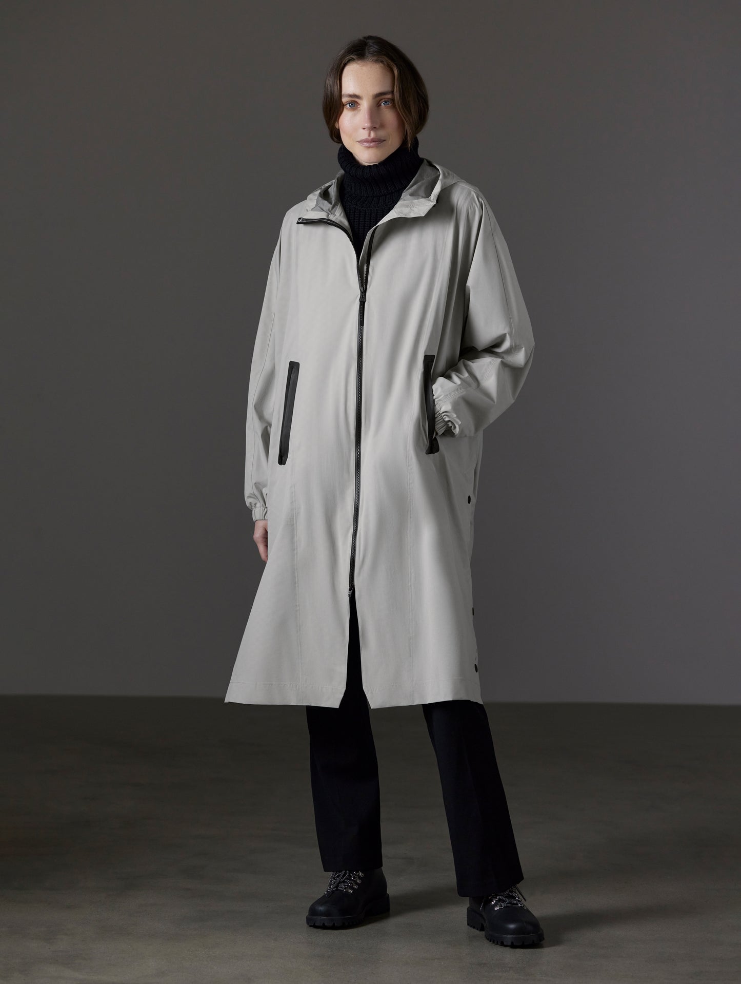Front angled full-body view of woman wearing Kite Packable Rain Poncho in Stone Grey from AETHER Apparel.