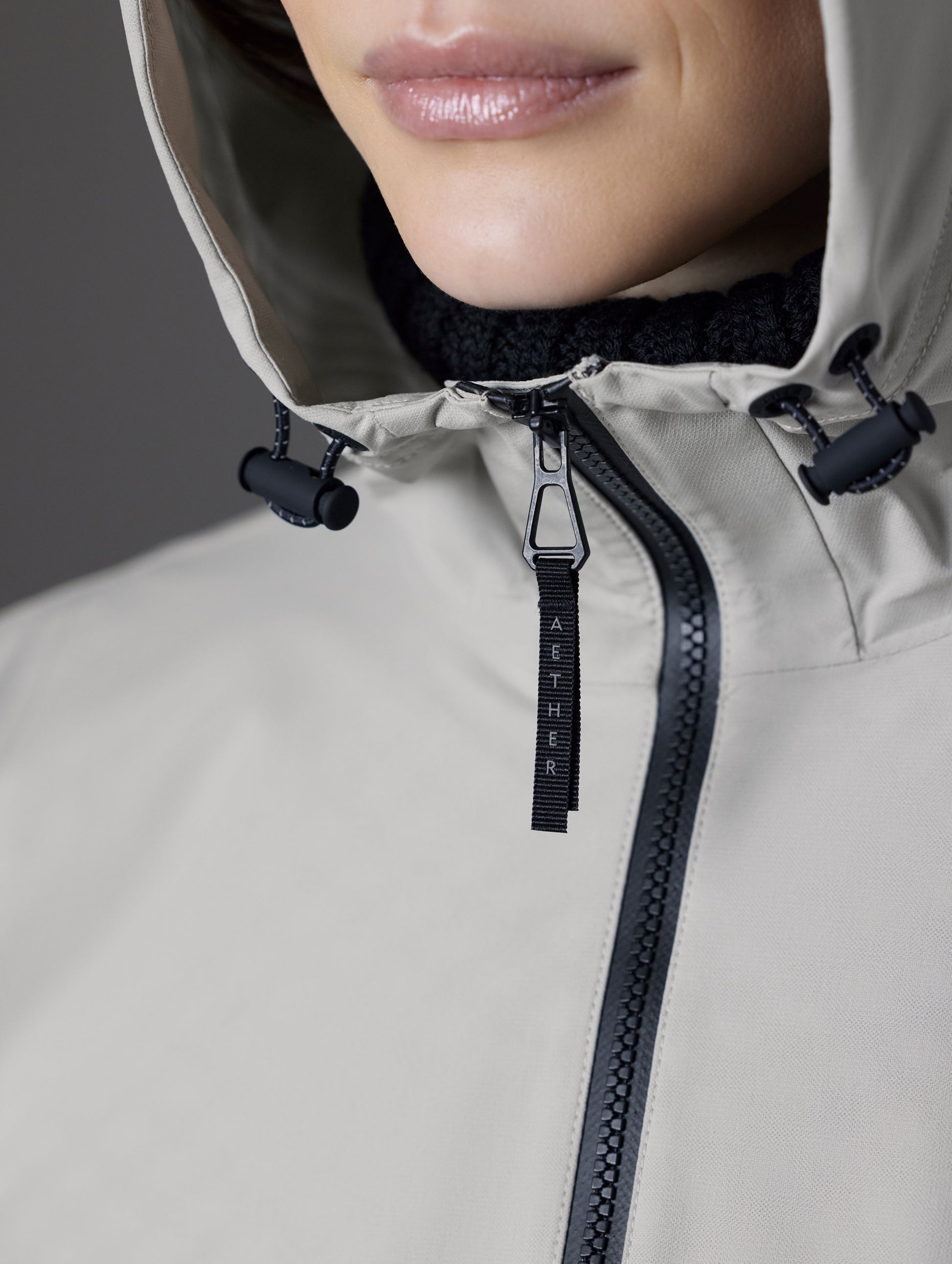 Closeup detailed view of the main center-front zipper and three-piece hood's bungee adjustments on the Kite Packable Rain Poncho in Stone Grey from AETHER Apparel.